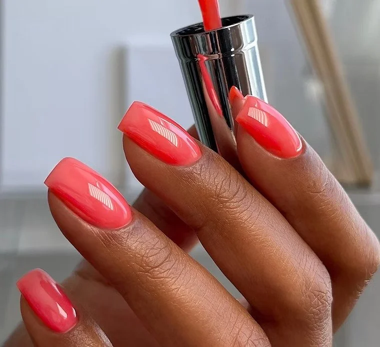 glossy coral gel manicure on Black hand with polish brush, highlighting smooth manicure application and shine