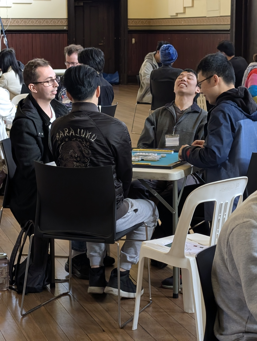Players sit at a table at Vic Riichi Open 2025 finding a comedic moment during a game