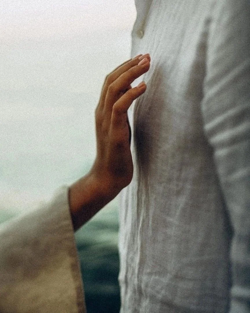 A person's hand touching a person's chest, dressed in a light-colored shirt.