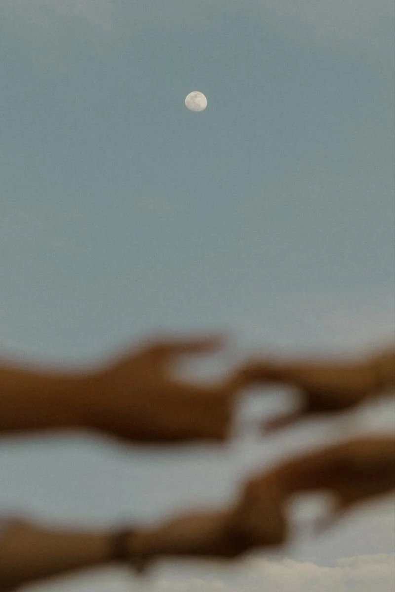 Blurred hands in the foreground with a clear moon in the sky in the background.