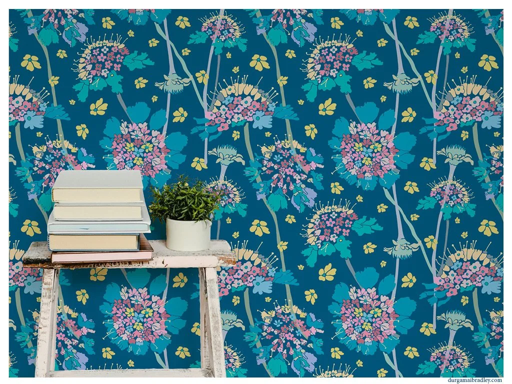 A rustic small wooden table with chipped white paint holding five stacked books and a potted green plant, set against a vibrant blue floral wallpaper background.