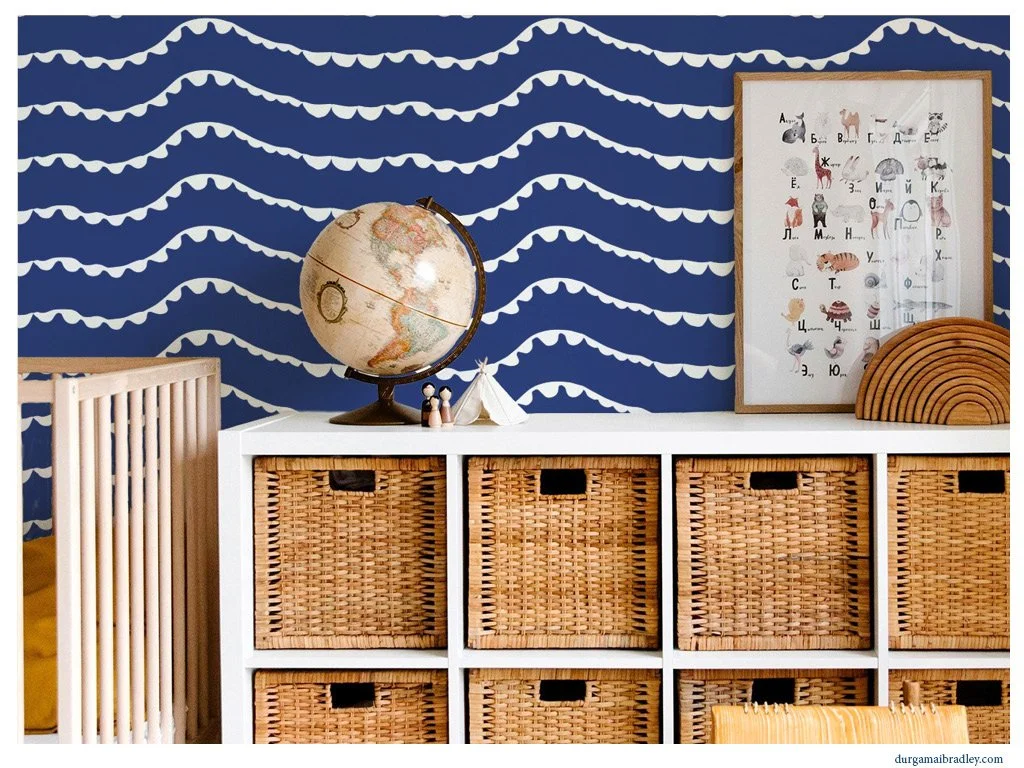 A child's room with a white storage unit containing woven baskets, a globe, framed animal alphabet print, and wooden decorations against a blue wall with white wave pattern.