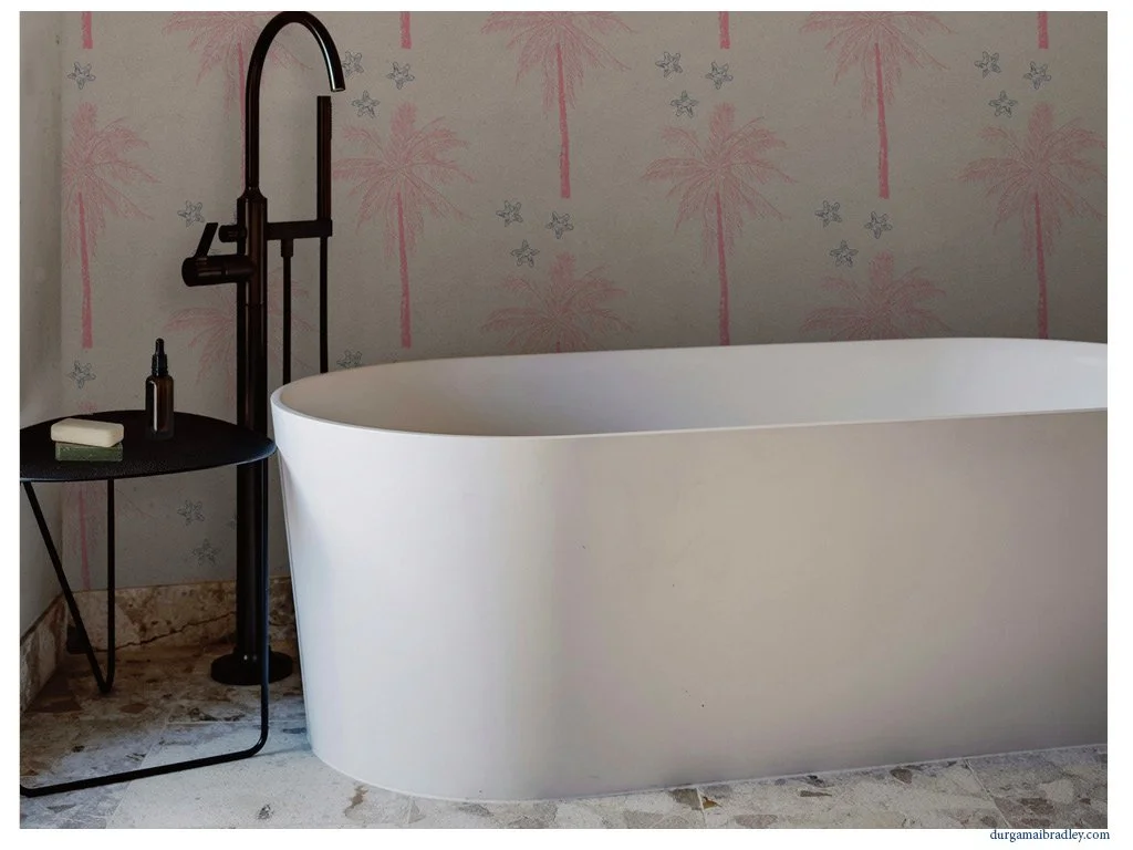 A modern bathroom with a free-standing, oval-shaped white bathtub, a black floor-standing faucet, and a small black side table holding toiletries. The background features light-colored wallpaper with pink palm trees and small butterflies.