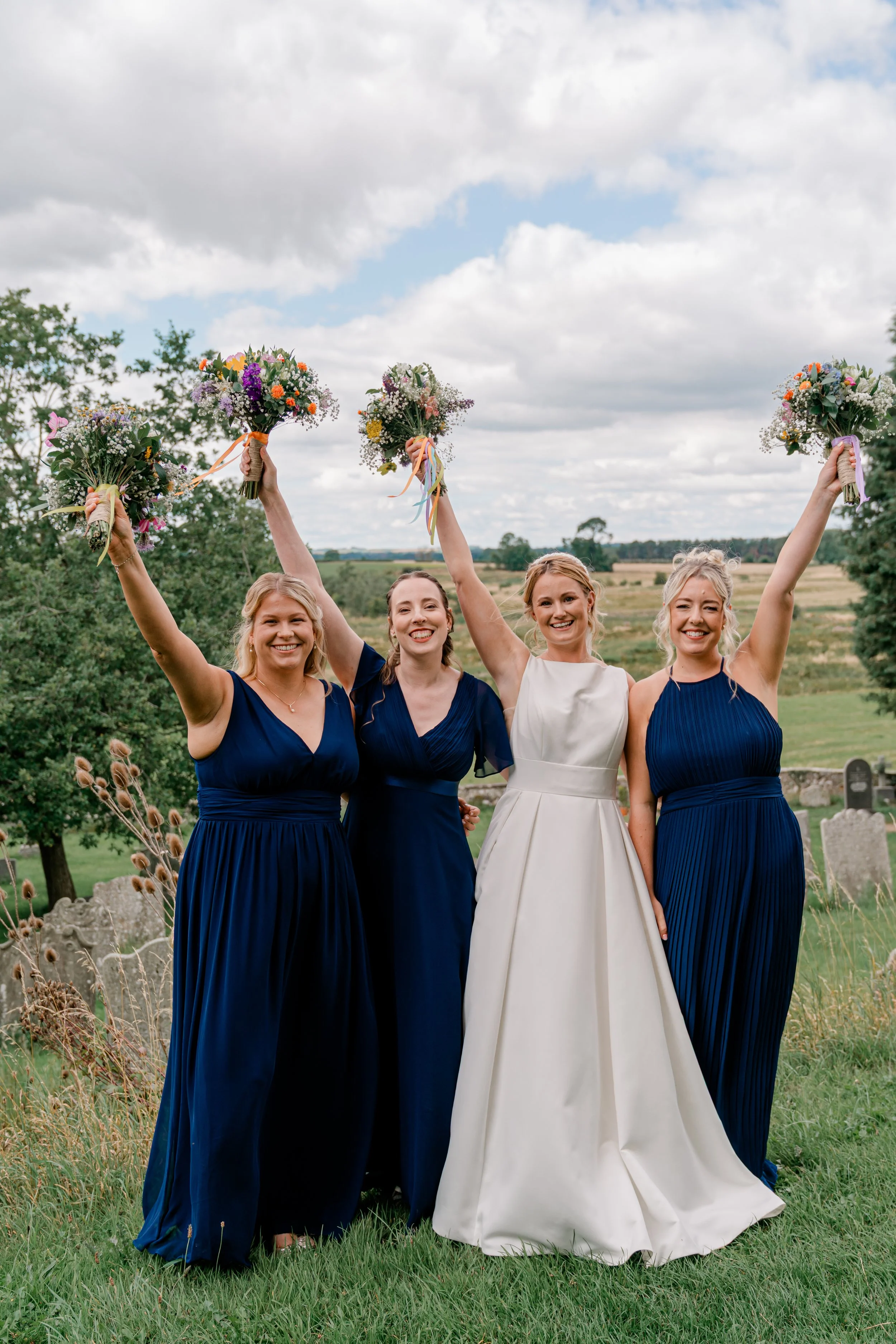Bridal party holding flowers in the air celebrating at church wedding in Northumberland, countryside wedding