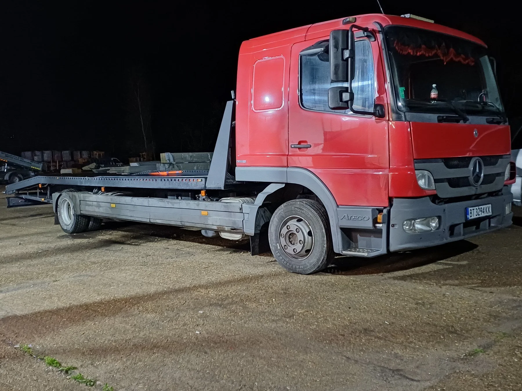 Red Mercedes-Benz tow truck parked on a dirt lot at night.