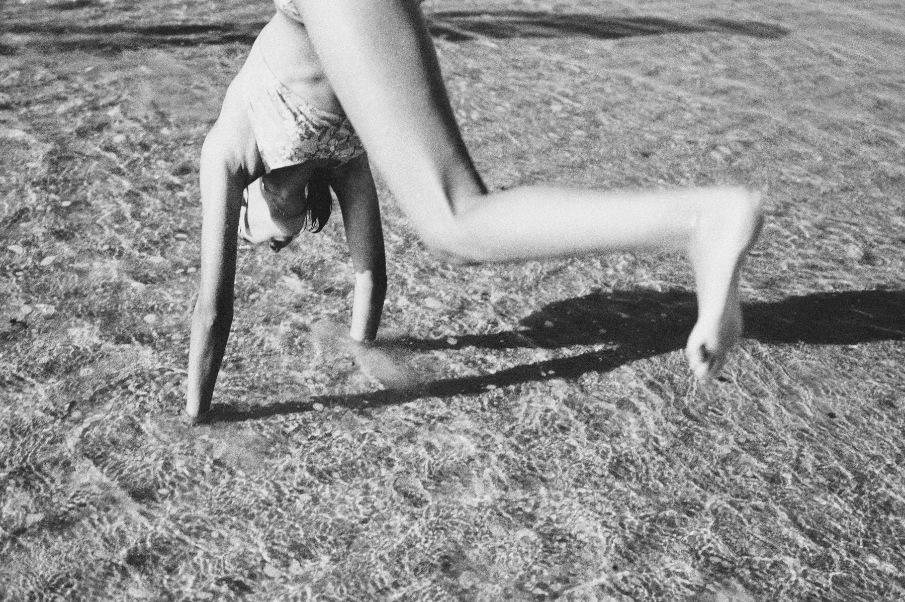 A blurry black and white photograph of a young girl doing a flip in the water.