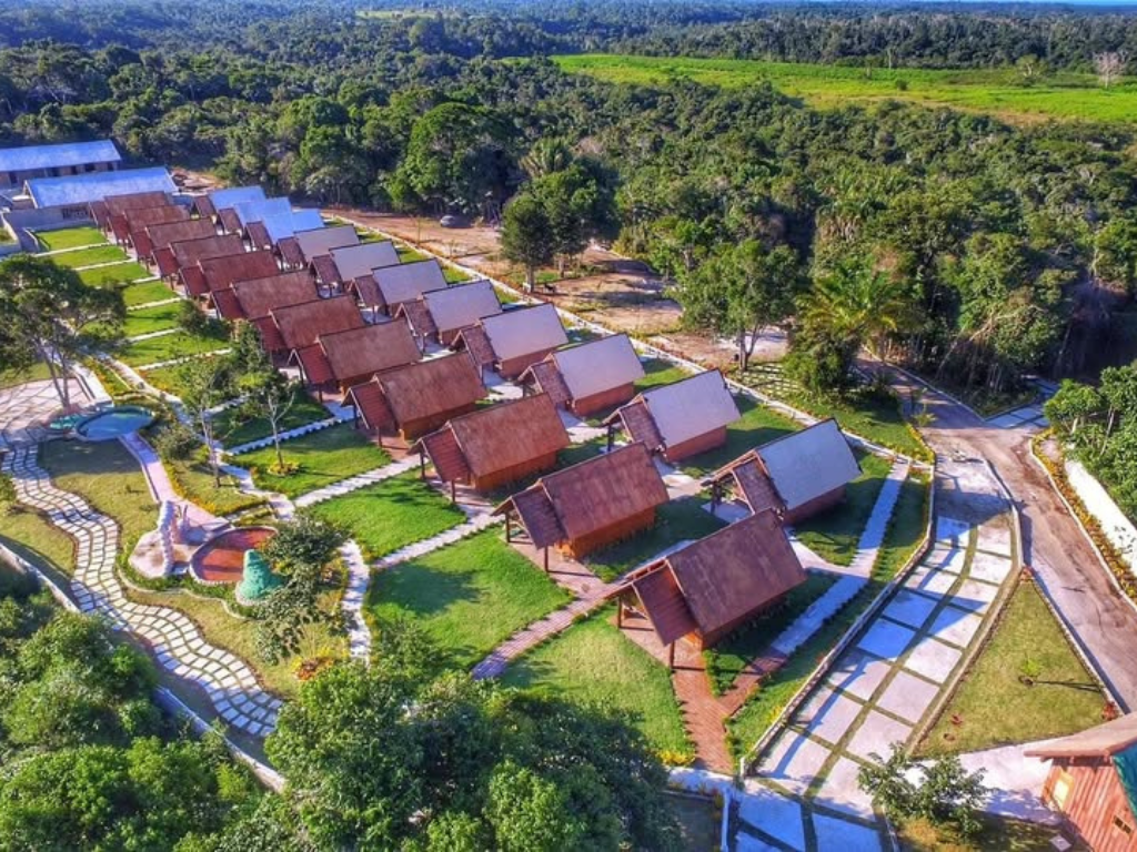 Vista aérea de chalés triangulares em um resort cercado por vegetação e caminhos pavimentados.