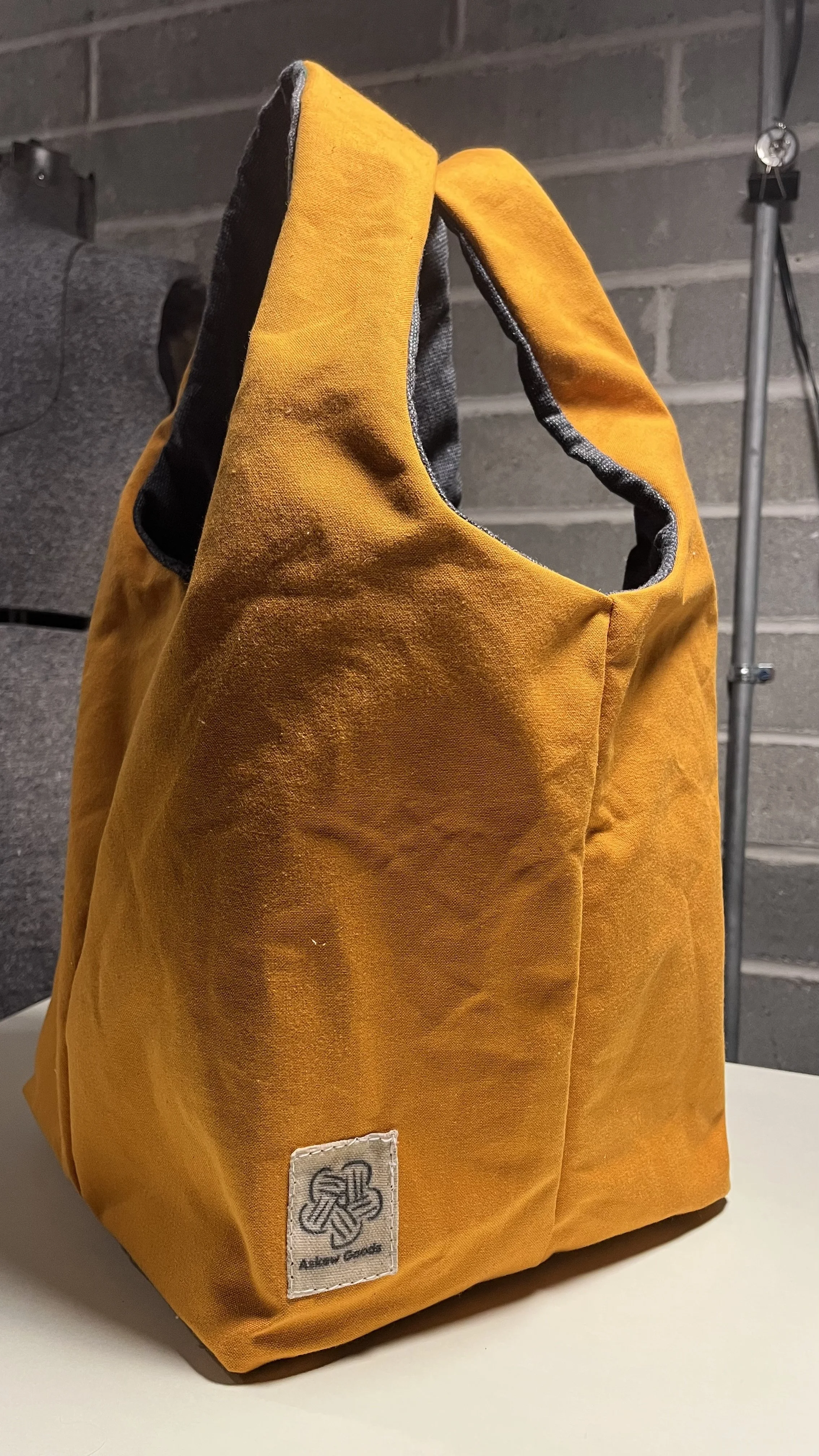 A yellow fabric tote bag hanging against a grey brick wall.