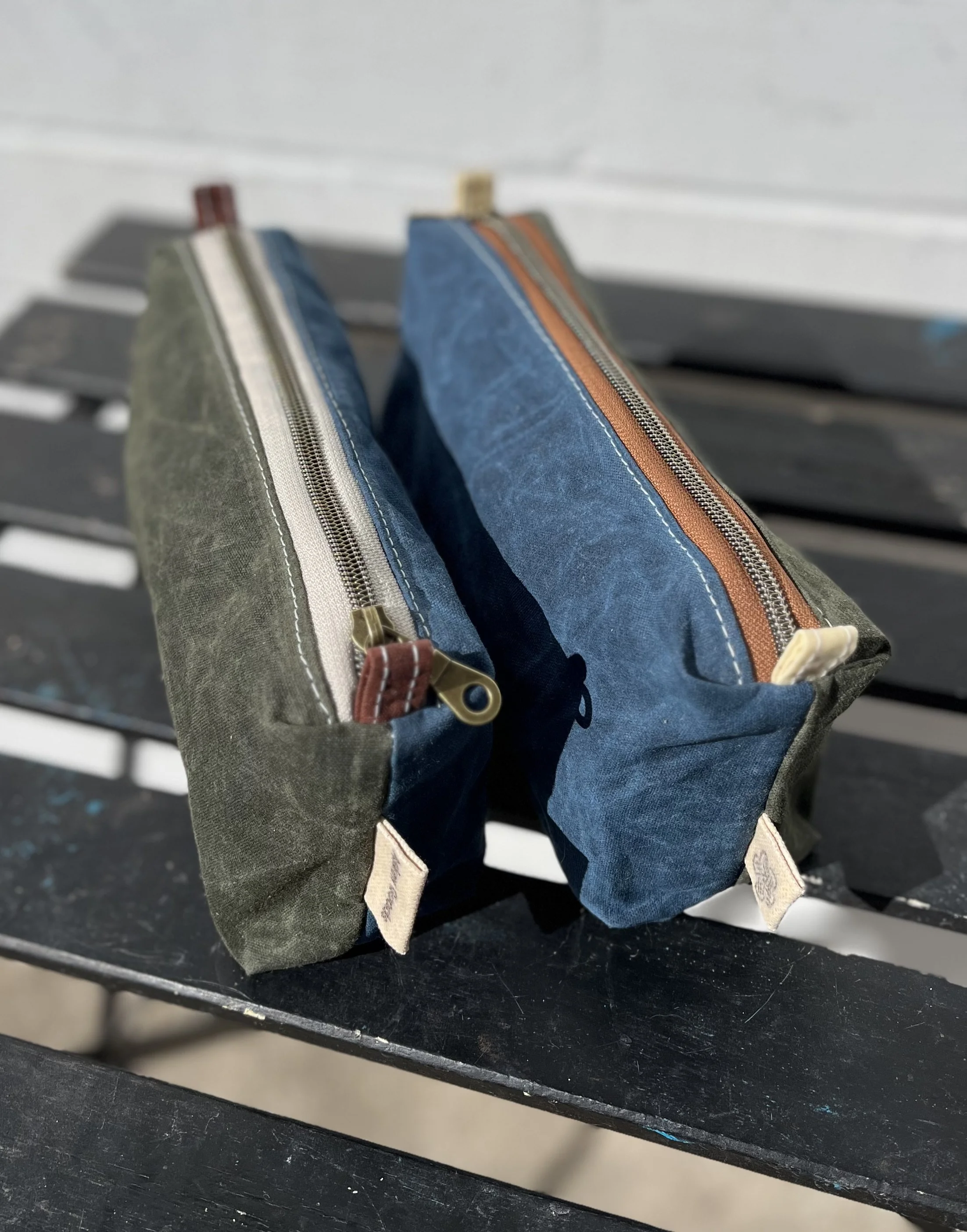 Close-up of four denim and colored fabric pencil cases with zippers, resting on a dark surface.