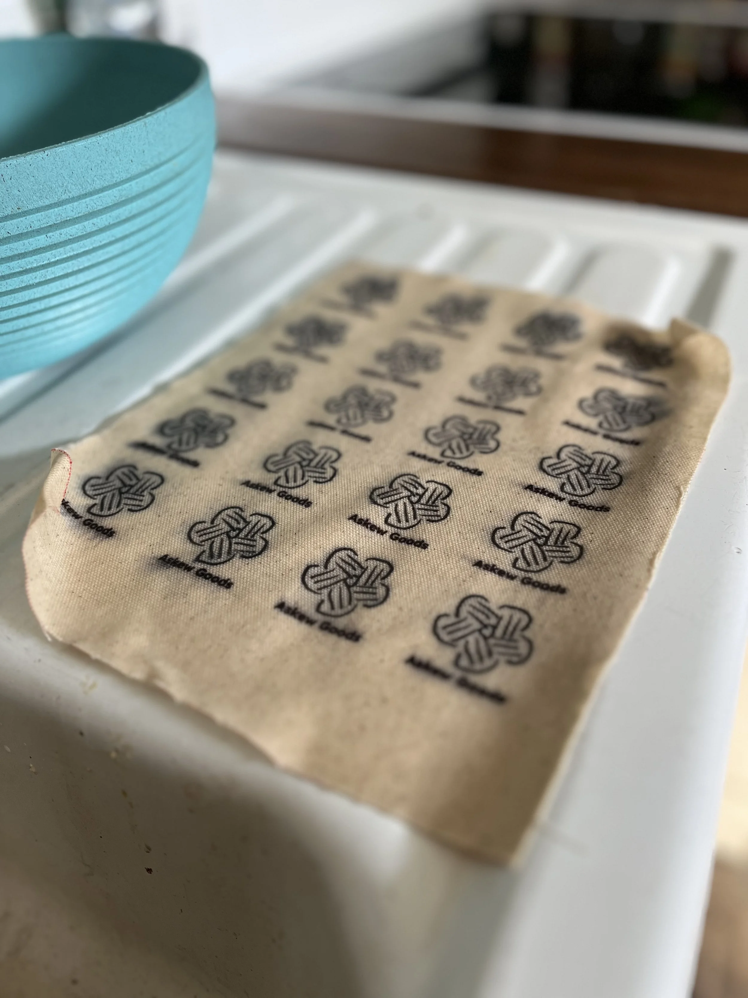 Close-up of a beige cloth with black printed logo patterns resting on a white surface, with a blue ceramic bowl in the background.