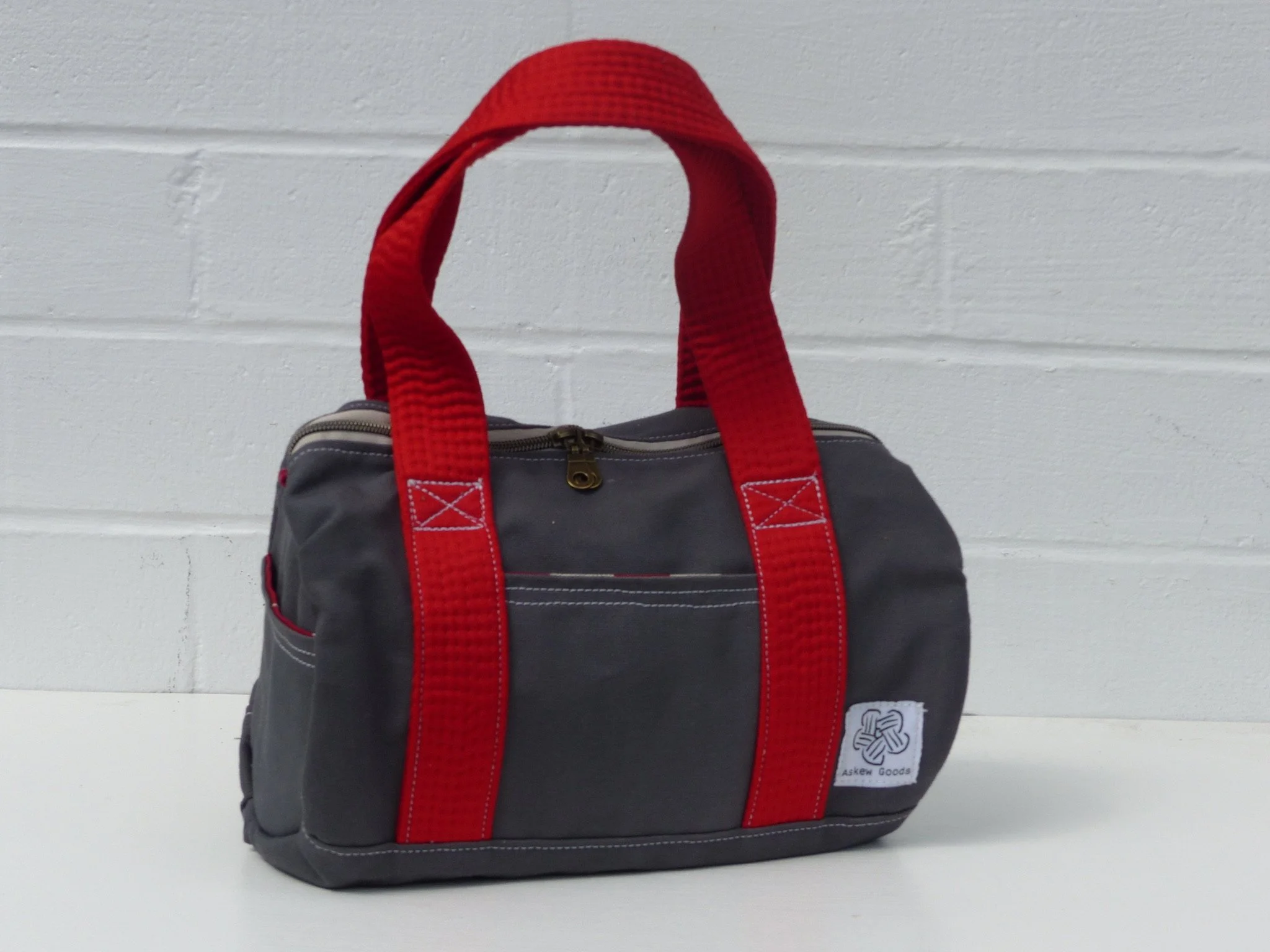 A black and gray backpack with red straps hanging on a white brick wall.