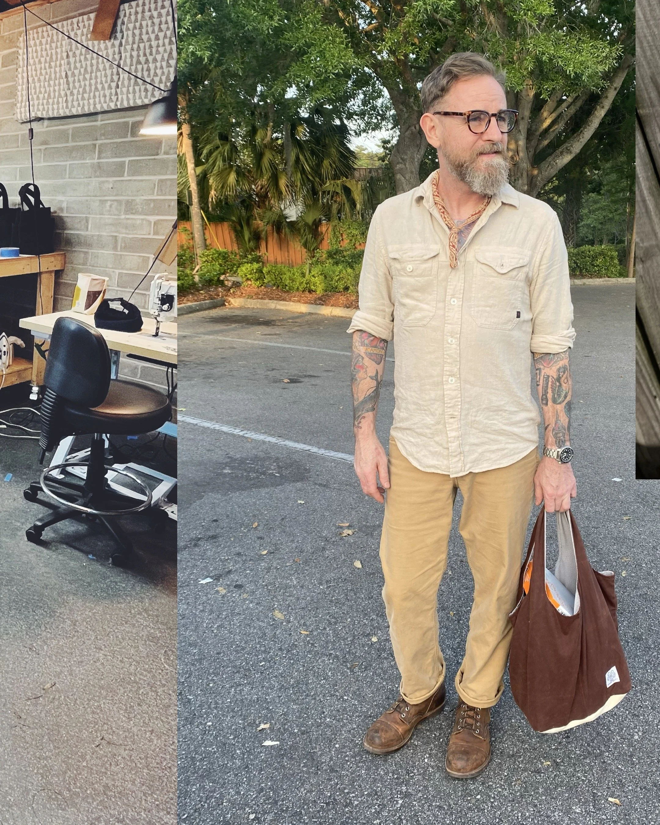 Man with tattoos in a beige shirt, beige pants, and brown boots standing outdoors with trees and a parking lot in the background, holding a brown shopping bag and a white grocery bag.