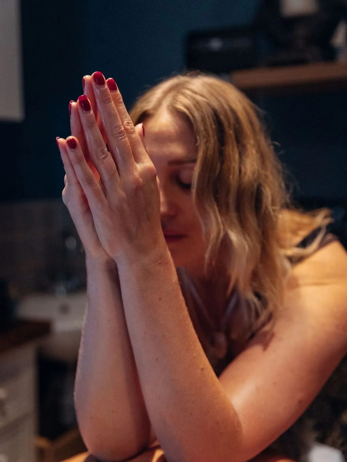 A woman with red hair and red nail polish with her hands pressed together in a prayer or meditative pose, eyes closed.