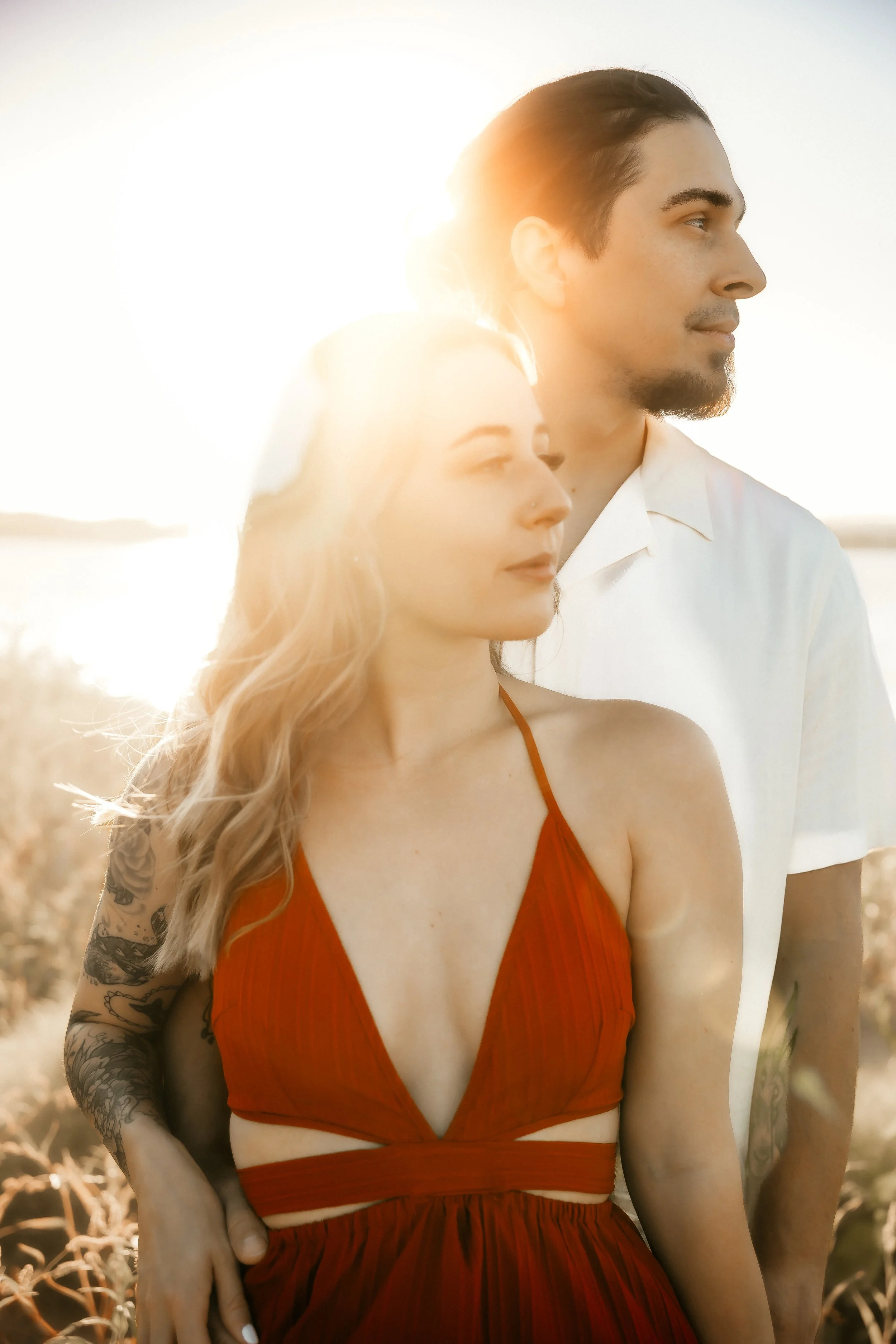 A man and a woman standing outdoors during sunset, with the sun behind them creating a silhouette effect.