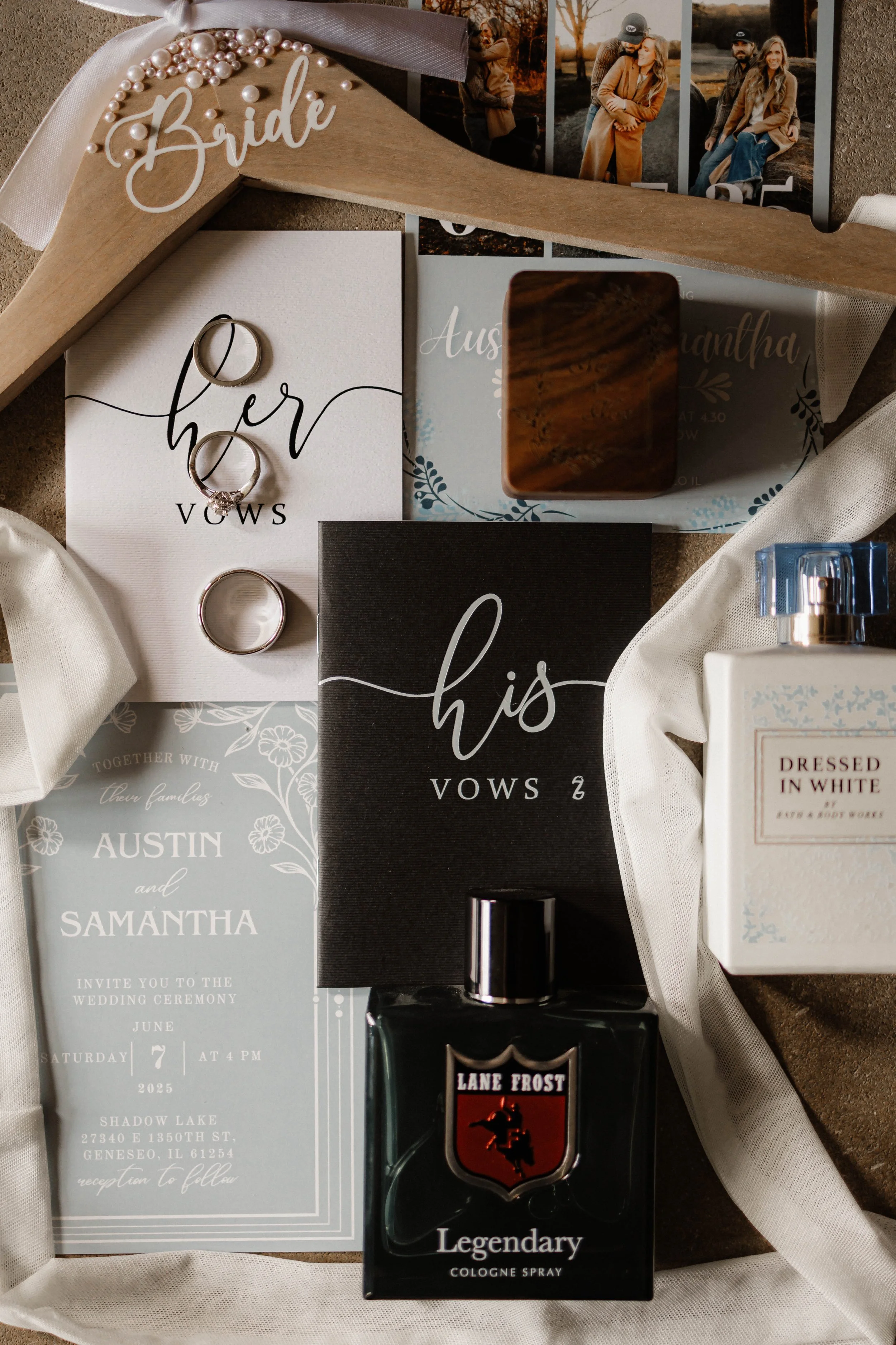 Wedding accessories including a bridal hanger with pearls and the word 'bride', wedding rings, vow booklets labeled 'her vows' and 'his vows', wedding invitation for Austin and Samantha, a bottle of Lane Frost Legend cologne spray, a box of Dressed i