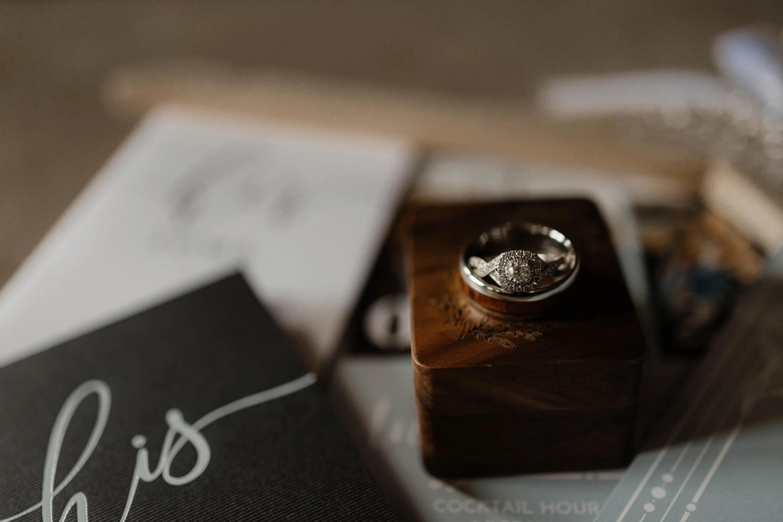 A diamond engagement ring placed on a wooden box, with a partially visible menu or booklet nearby.