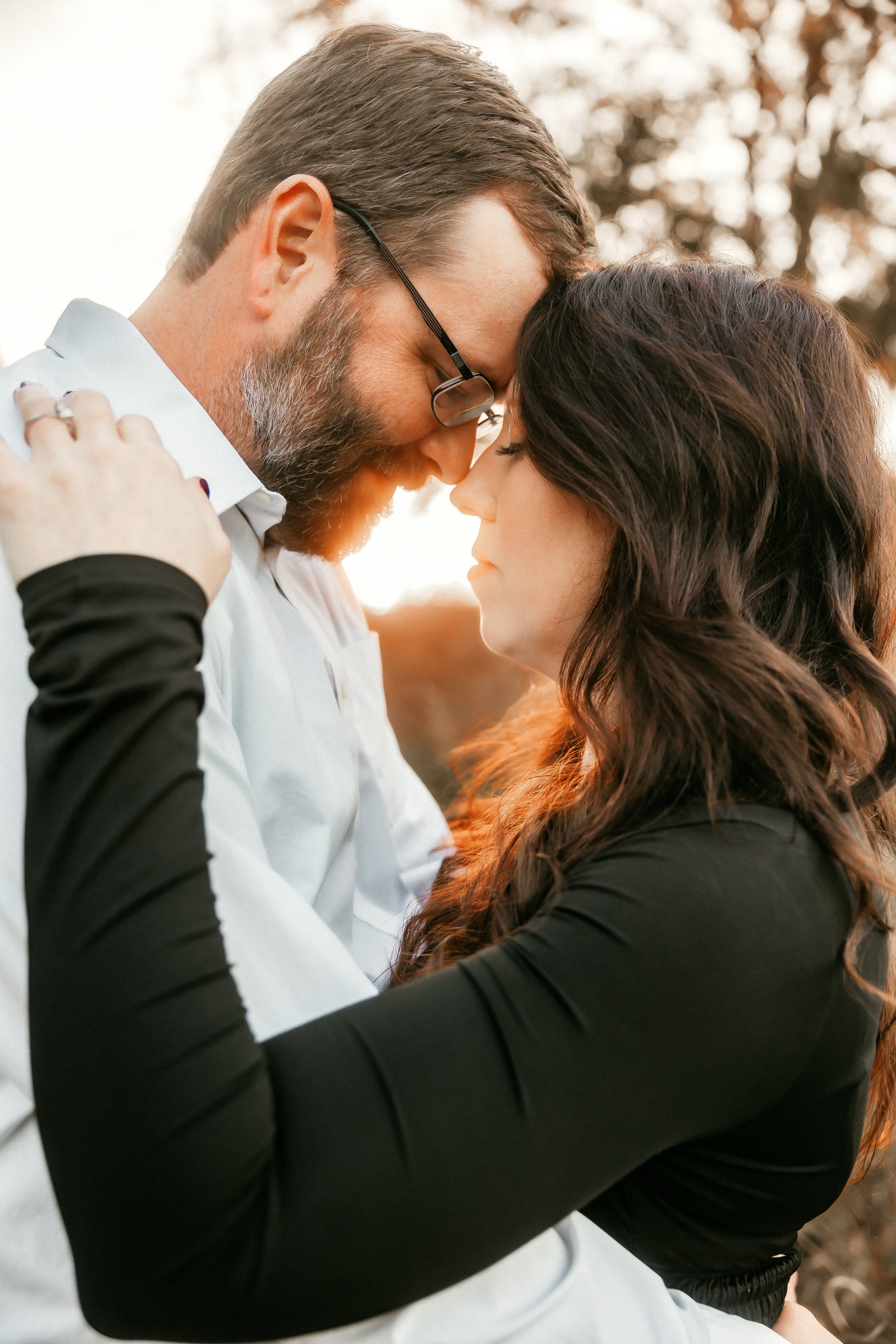 A couple touching foreheads and holding each other, outdoors during sunset.