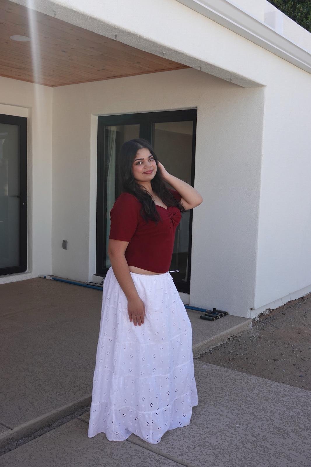 A woman in a red top and white skirt standing outside a modern house with large glass doors.