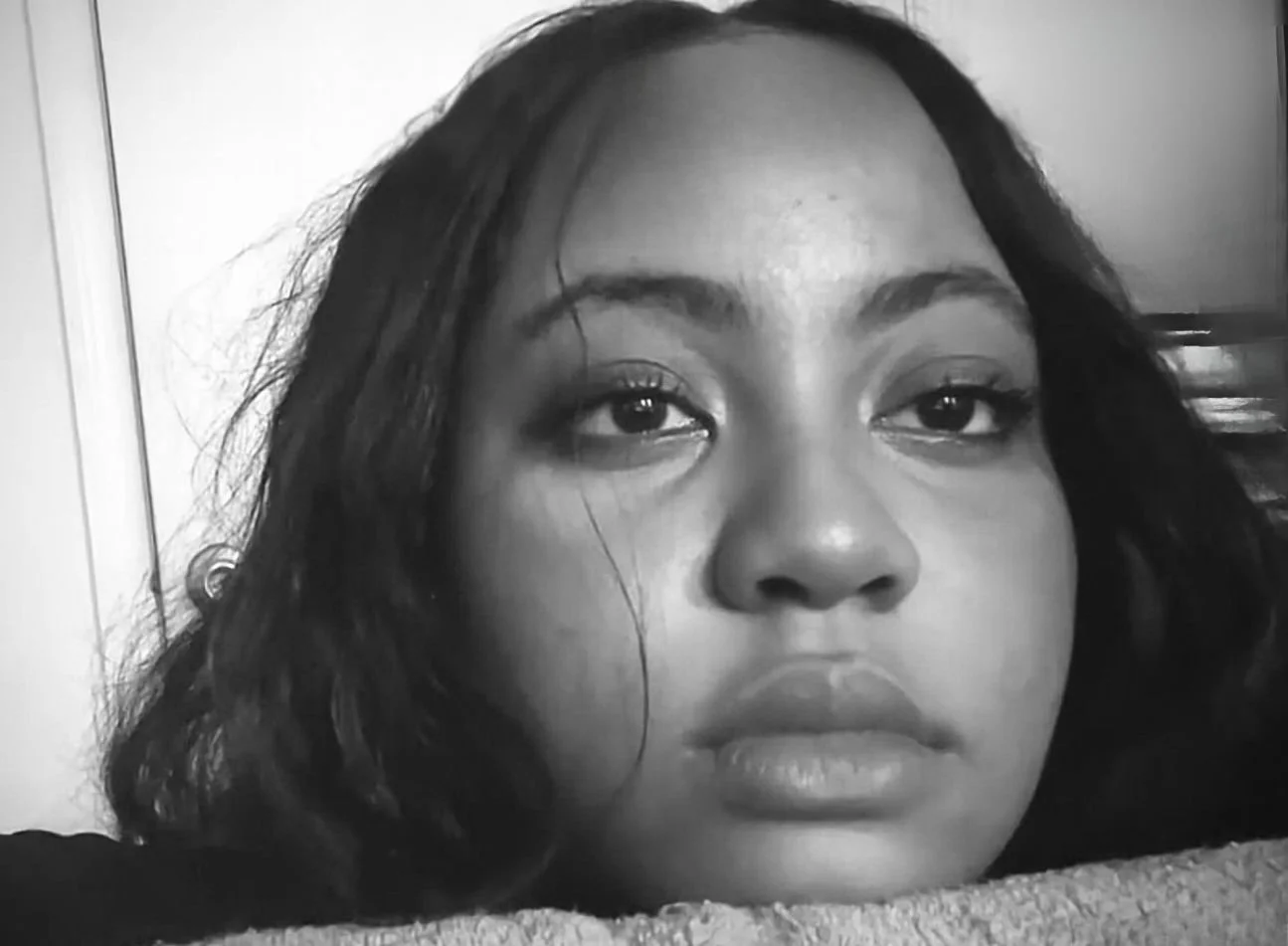 Close-up black and white portrait of a woman with medium-length dark hair resting on a surface, looking directly at the camera.