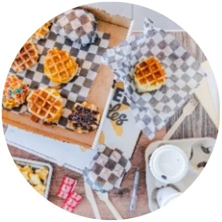 Assorted mini waffle sandwiches and condiments on a table with checkered parchment paper.