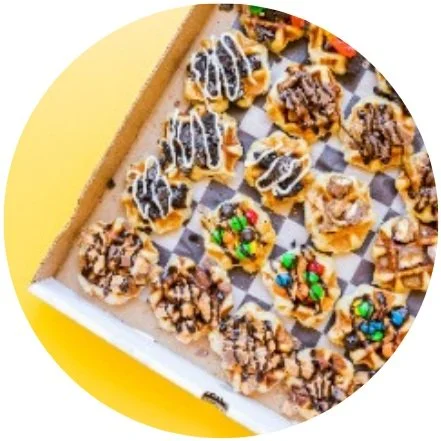 Assorted mini waffles with various toppings in a box on a yellow background.