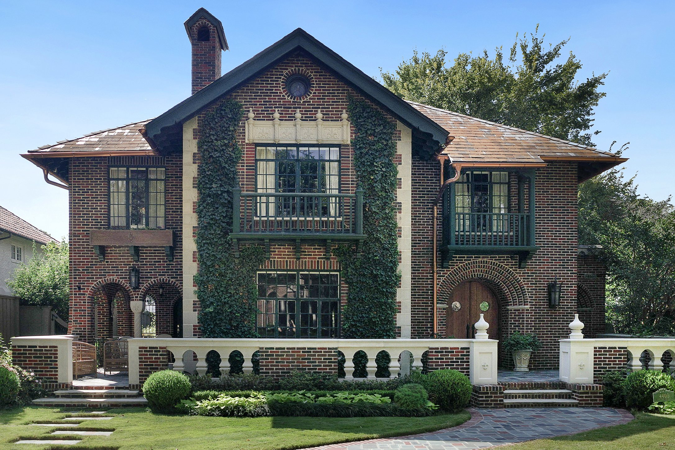 A two-story brick house with vine-covered walls, arched windows, a small balcony, and a landscaped front yard.