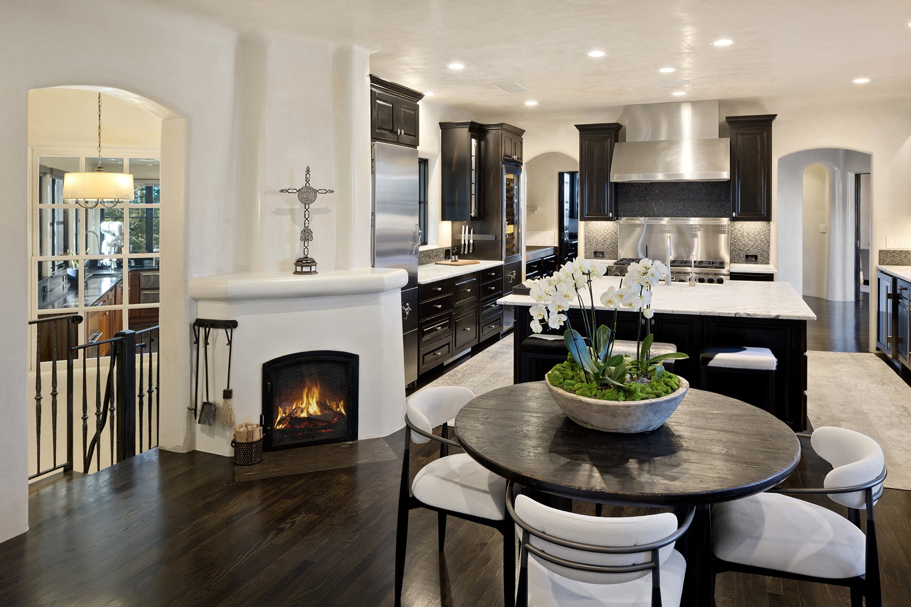 Modern kitchen with dark wood cabinetry, marble countertops, stainless steel appliances, a small fireplace, and a round dining table with white chairs.