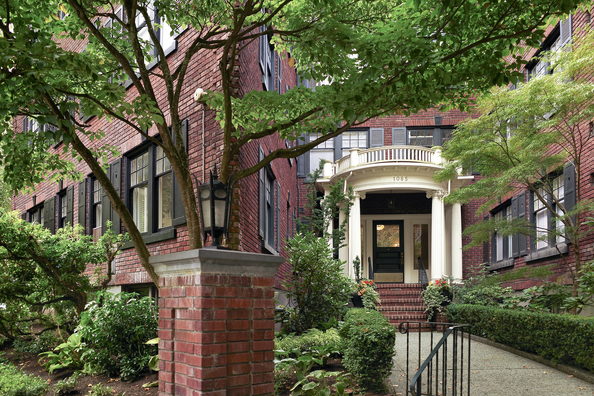 Brick apartment building with white columns, black shutters, and landscaped entrance.