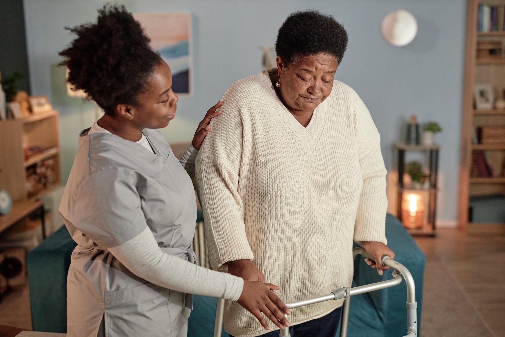 A caregiver assisting an elderly woman using a walker in a living room.