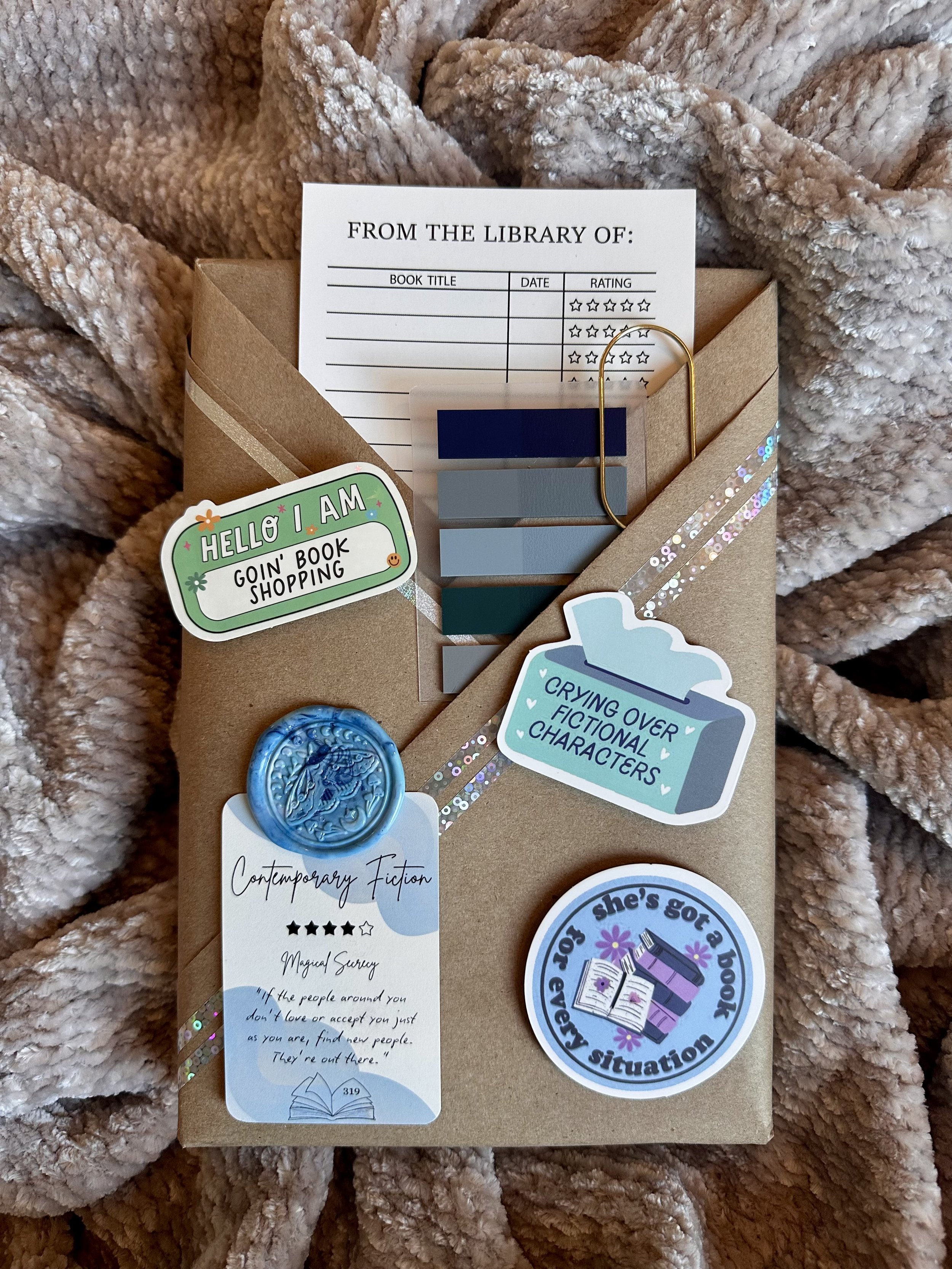 A Blind Date with a Book Bundle featuring a surprise book wrapped in brown paper with a hint card. Includes bookmarks, stickers, annotating strips, wax seal, and more.