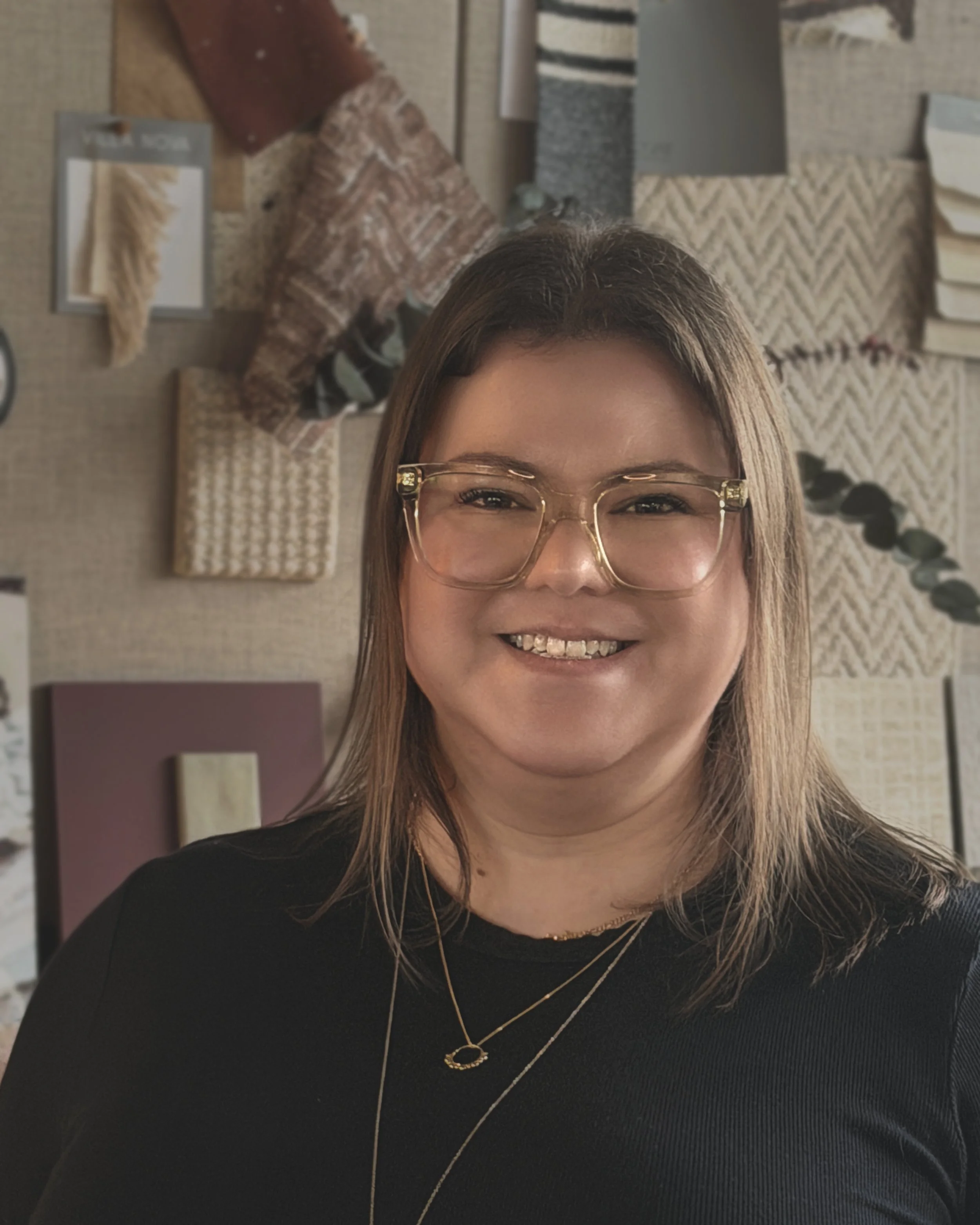 A professional female interior designer at a top interior design studio with brown hair and black jumper standing in front of a mood board.