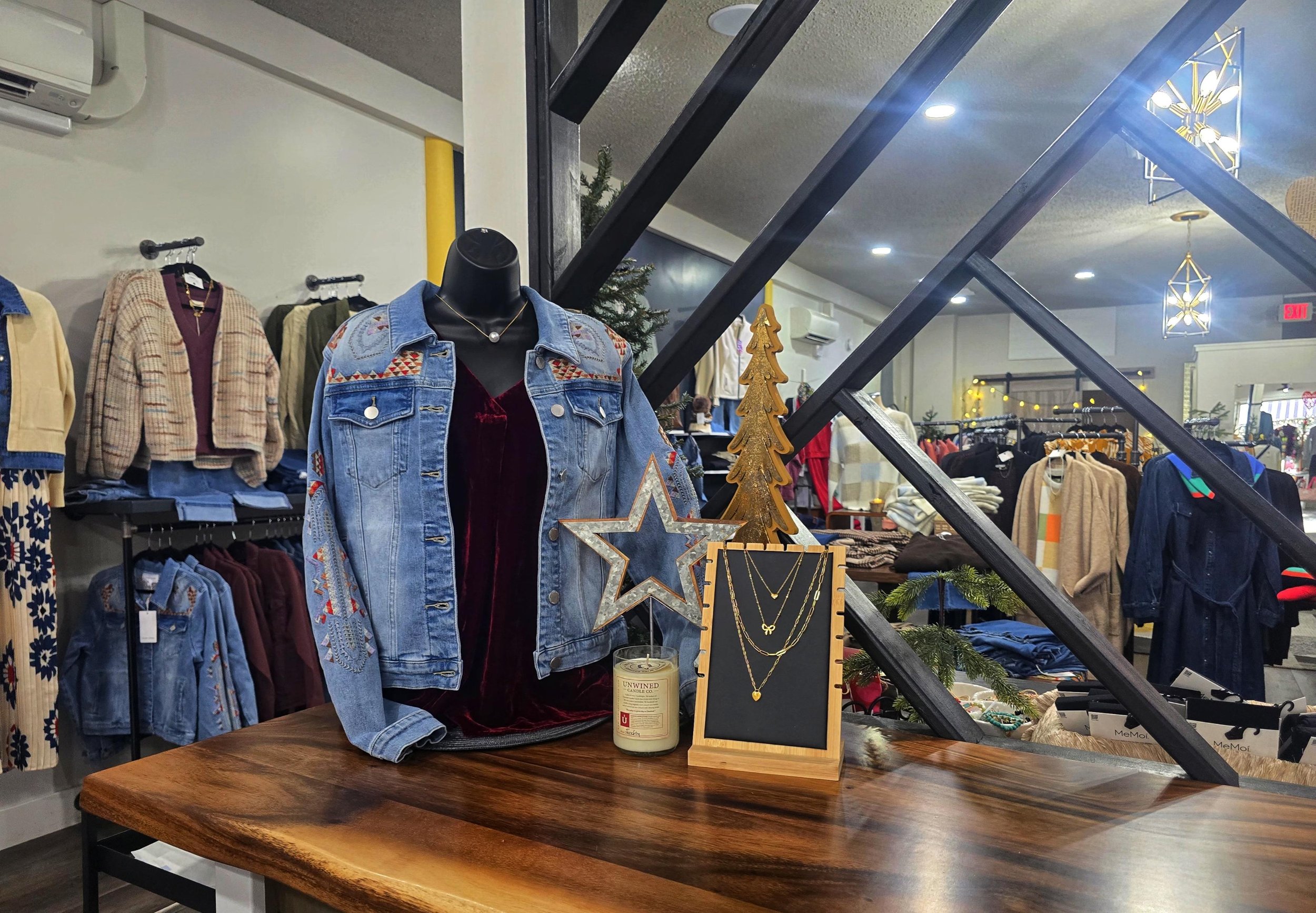 Display of denim jackets with embroidered details and layered necklaces in a clothing store holiday display.