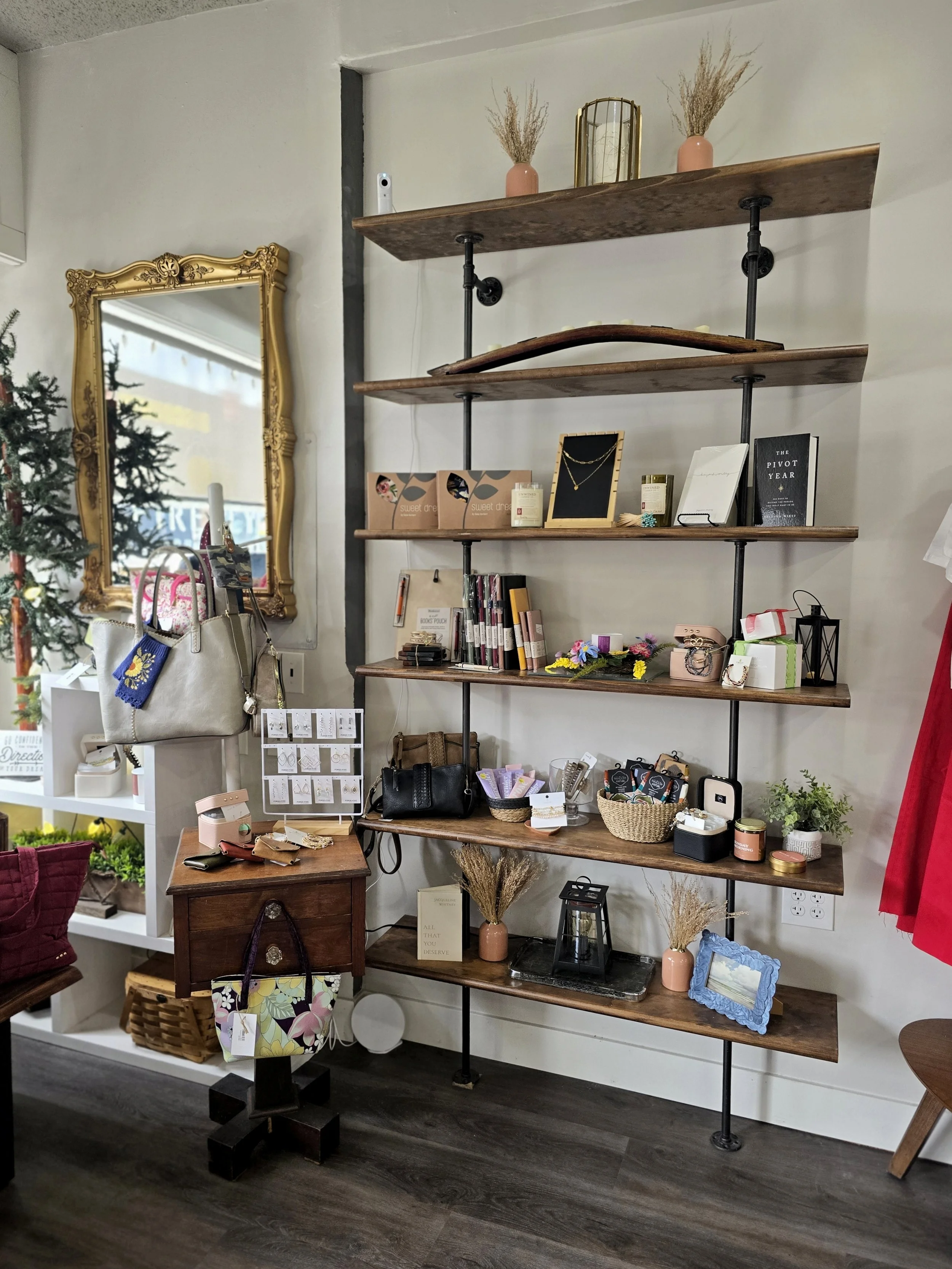 Display of handbags, jewelry, candles, picture frames, and small decor items on wooden and white furniture in a boutique store.