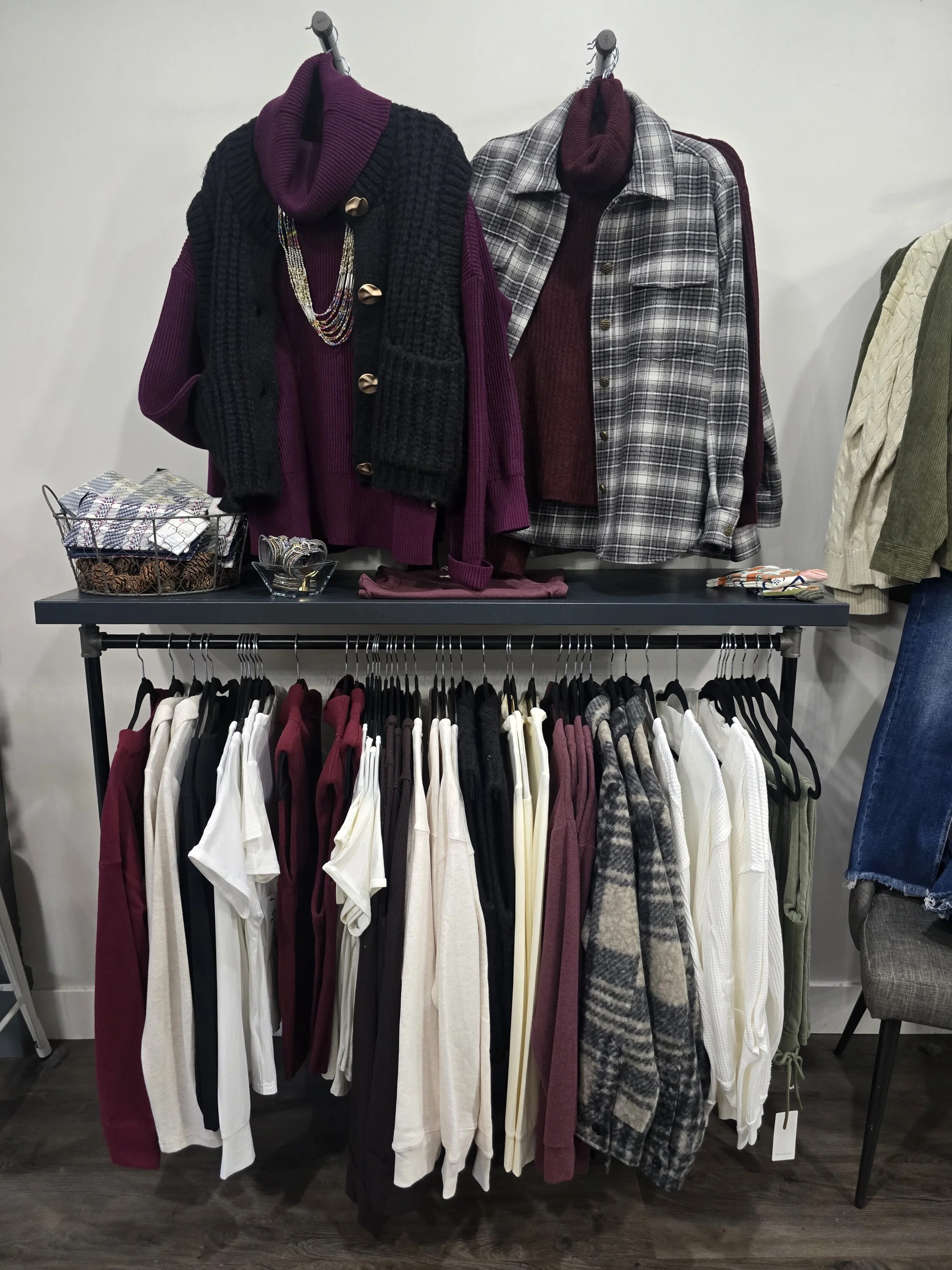 Display of hanging clothing items including sweaters, shirts, and scarves in a retail store.