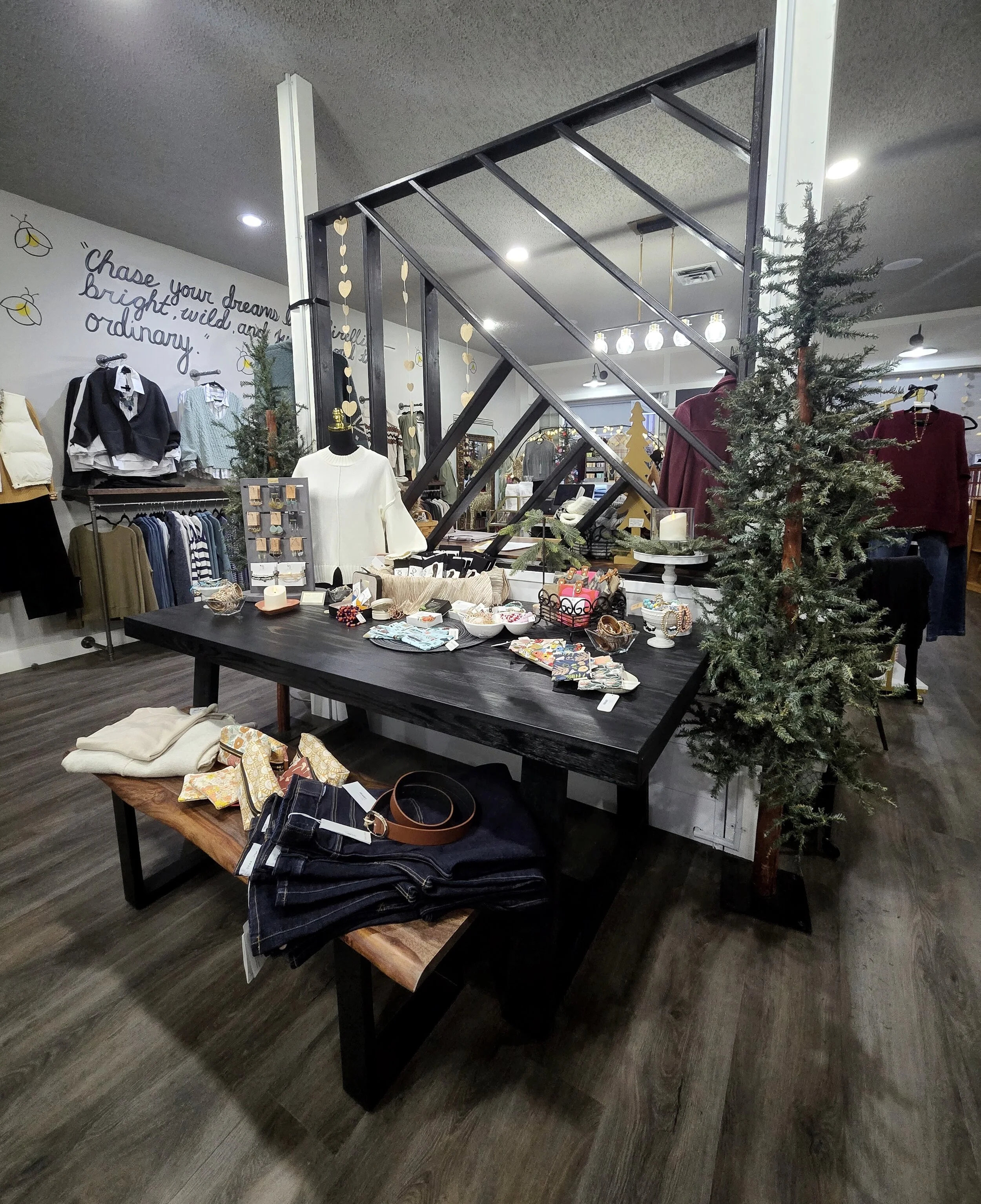 Display table with jewelry, accessories, and small items inside a clothing boutique, with Christmas trees and decorations around.