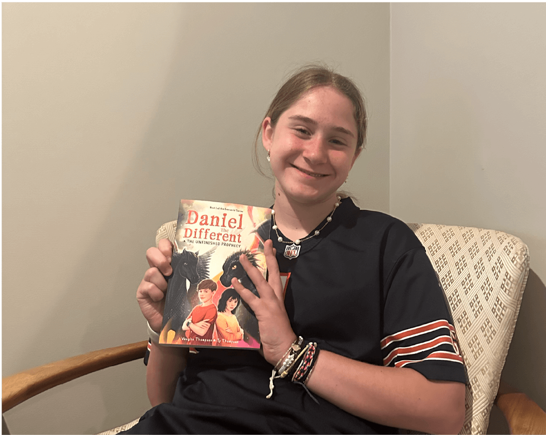Photo of girl smiling holding Daniel the Different book while sitting in chair