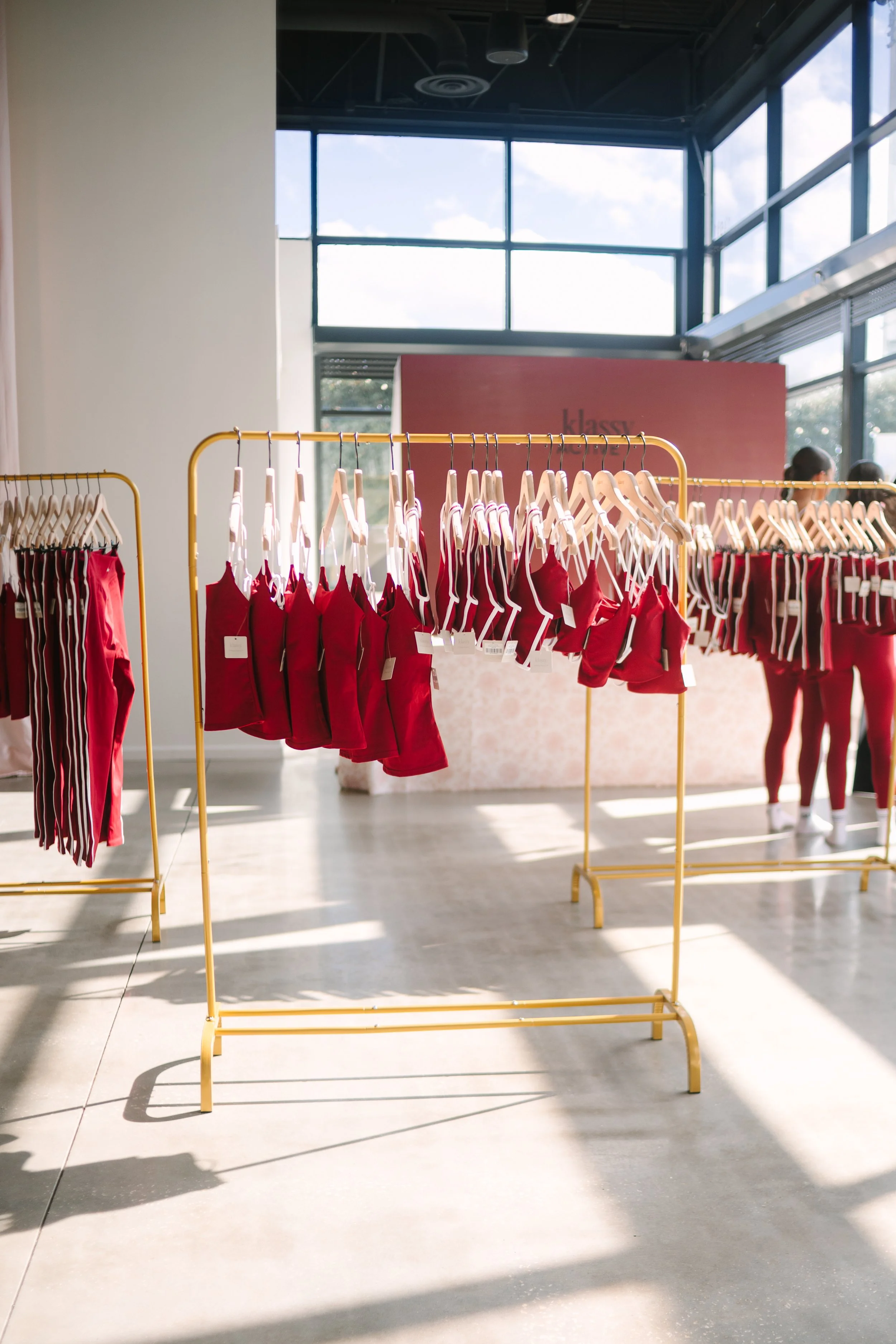 Display of red athletic shorts and pants hanging on gold racks in a bright retail store. Barre to Brunch with Jenna Palek