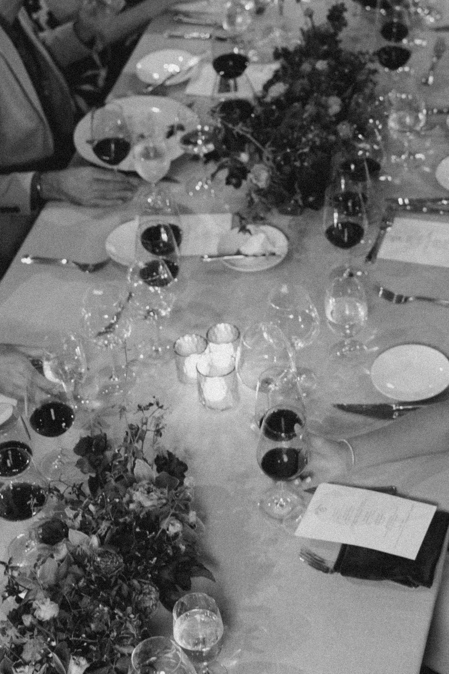 A table set for a formal dinner with wine glasses, plates, silverware, floral centerpieces, candles, and a menu or program.