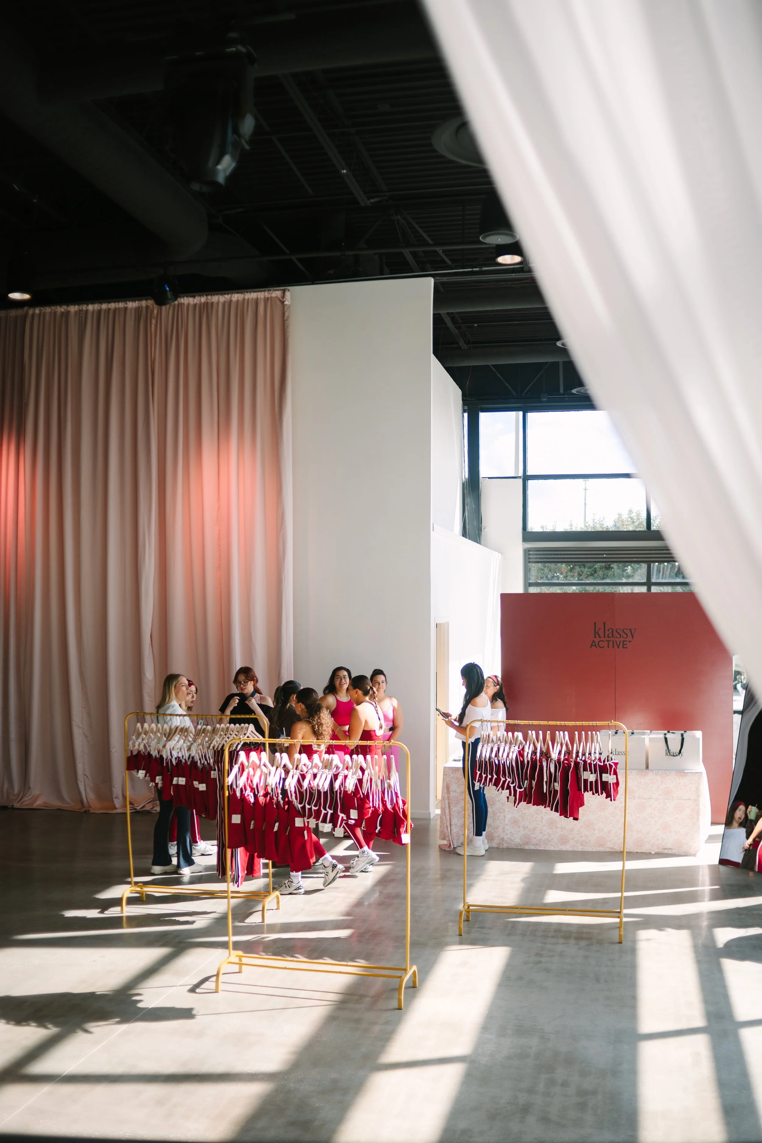 People shopping for pink and white clothing at a retail store with racks of clothes and a pink display area. Barre to Brunch with Jenna Palek