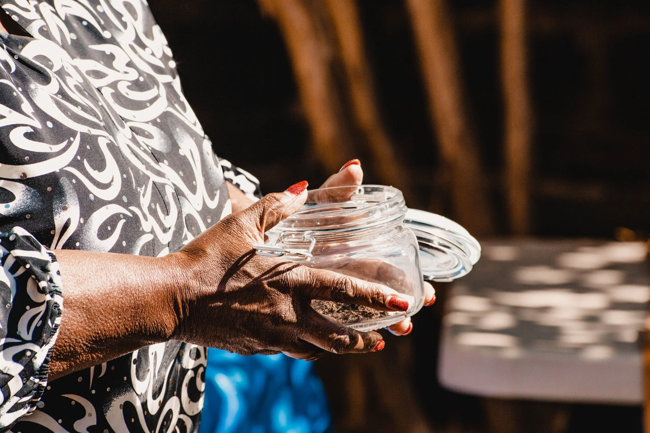 hands with aged dark brown skin bright red manicure holding jar of soil