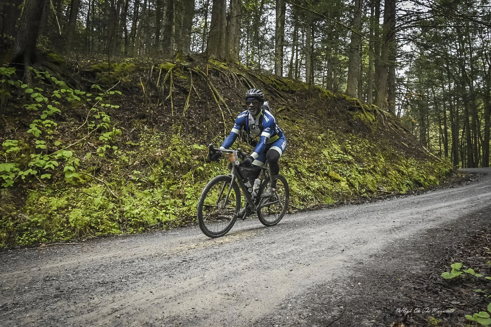 A person riding a bike on a gravel trail in a forest with green trees and moss-covered ground.