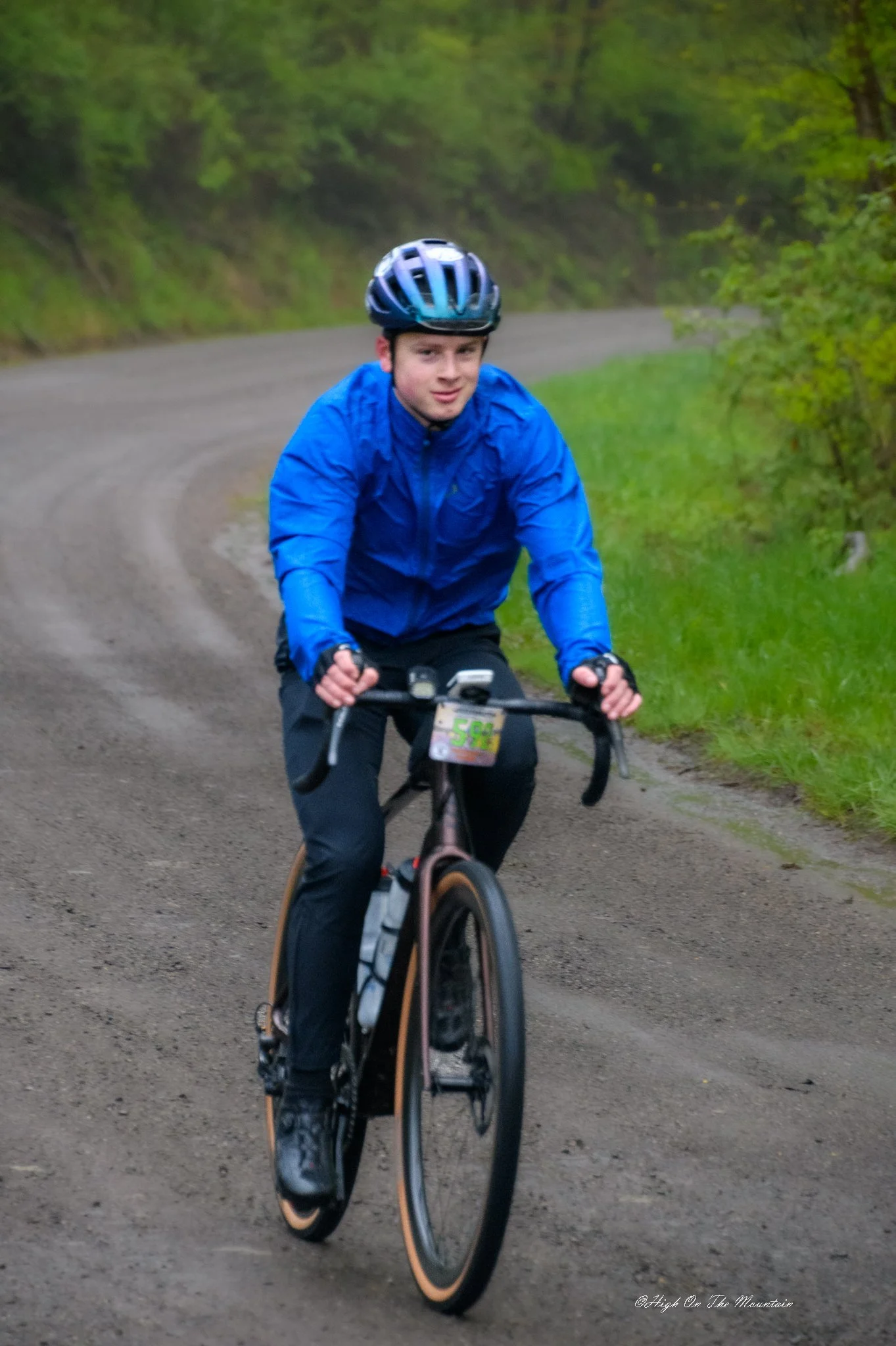 A young man cycling on a dirt trail surrounded by greenery and trees.