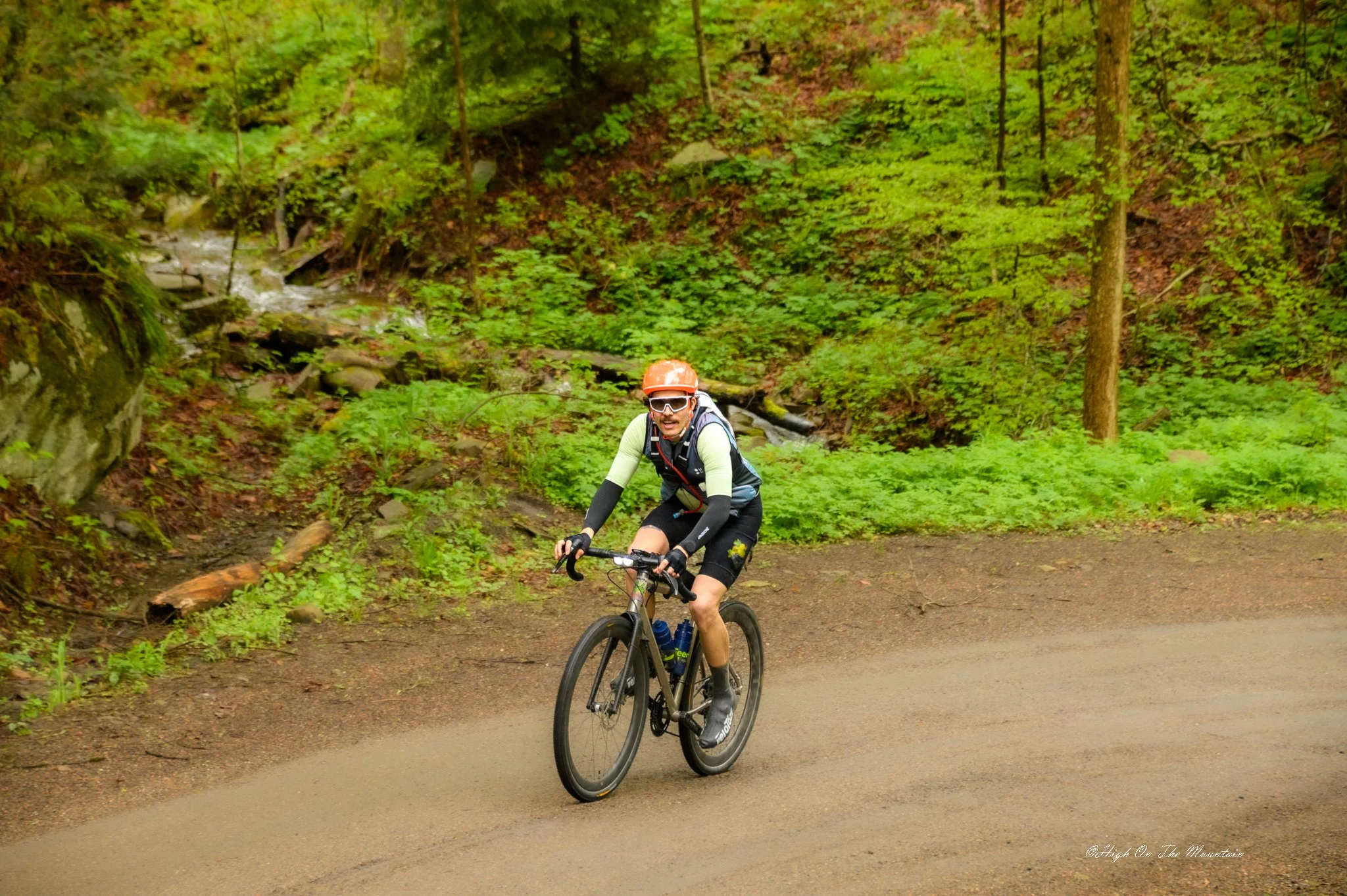 A person riding a mountain bike on a trail in a forest with lush green trees and bushes.