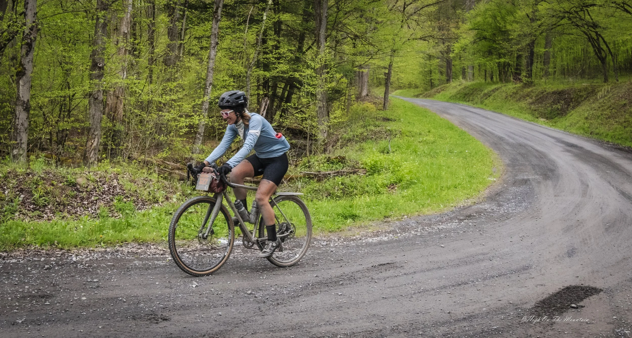 A woman riding a mountain bike on a gravel road through a lush green forest.