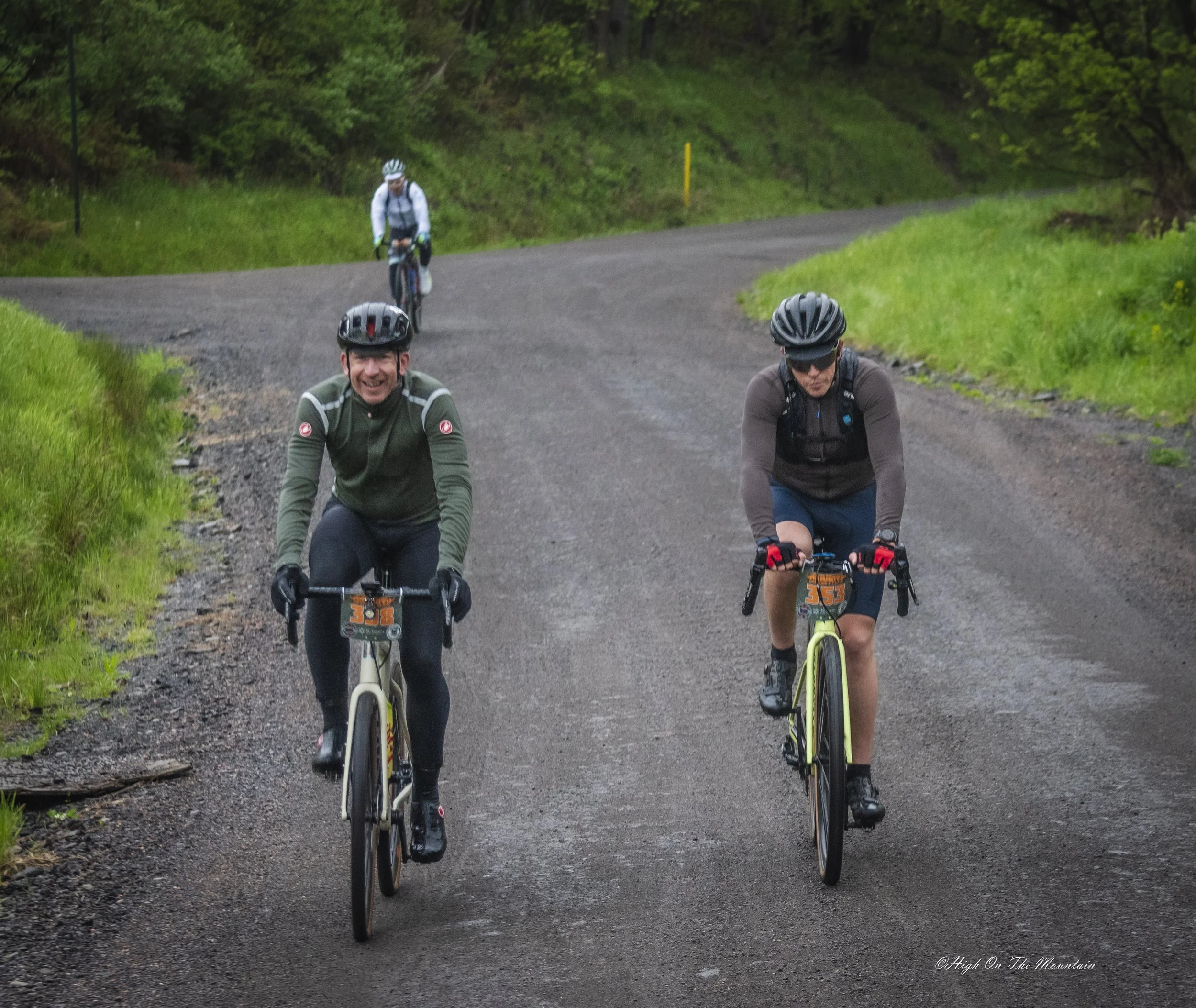 Four cyclists riding on a gravel path surrounded by greenery and trees.