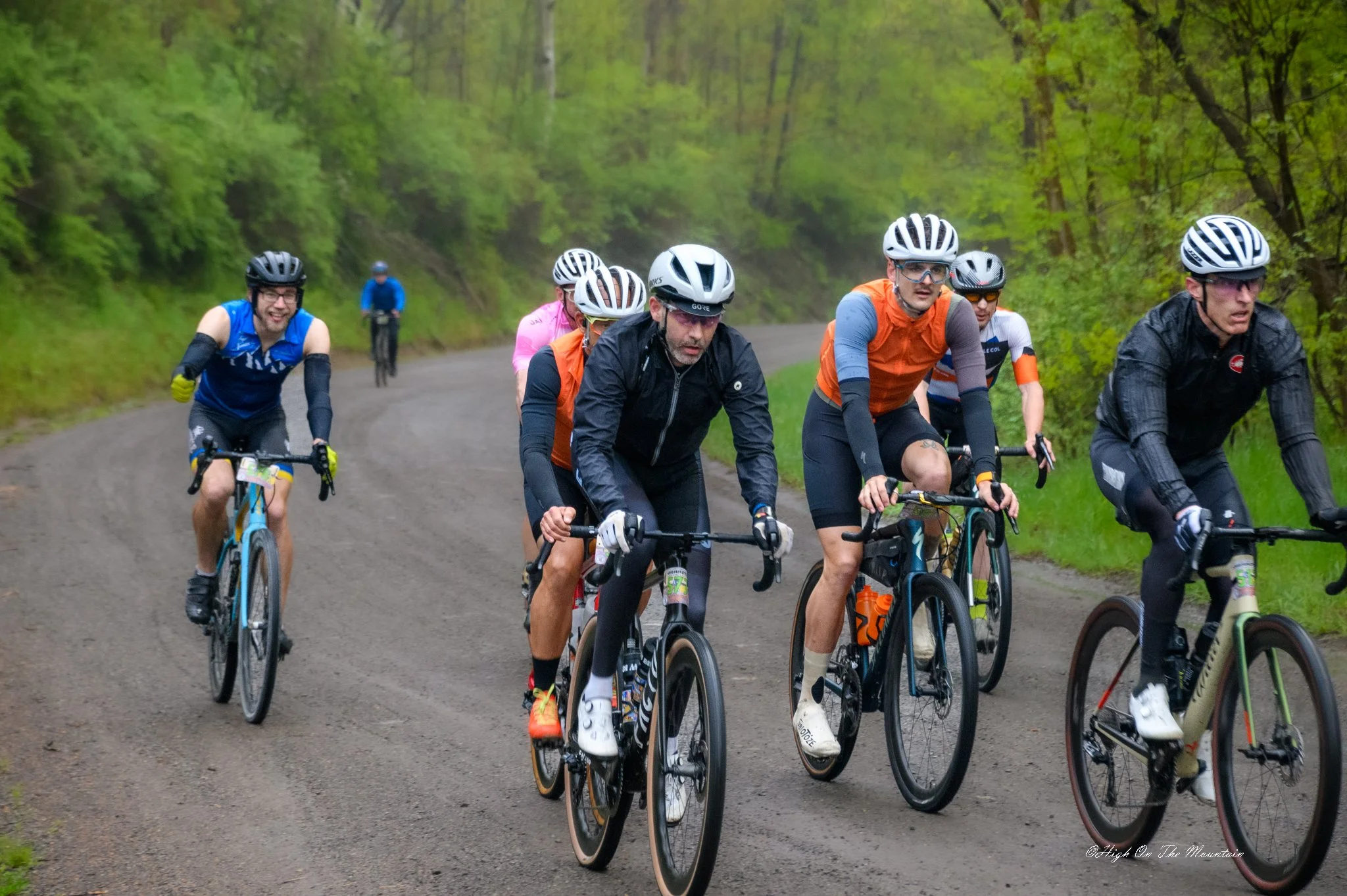 A group of cyclists riding on a forest trail surrounded by green trees.