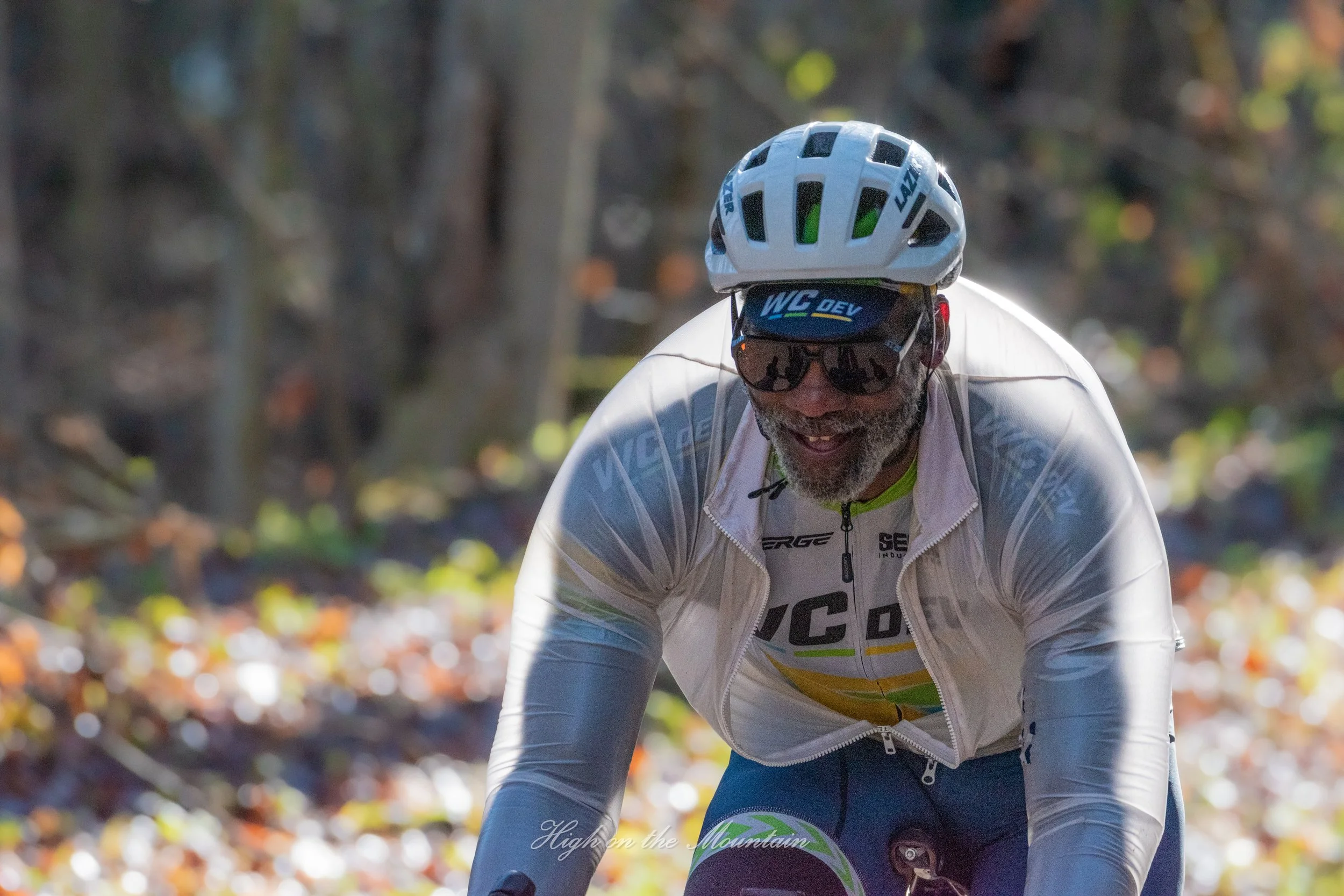 A cyclist wearing a white helmet and sunglasses rides on a trail with autumn leaves in the background.