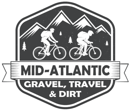 A black and white logo featuring two cyclists riding mountain bikes in front of a mountainous landscape with pine trees. Below, a banner with the text 'MID-ATLANTIC' and the words 'GRAVEL, TRAVEL & DIRT' beneath it.