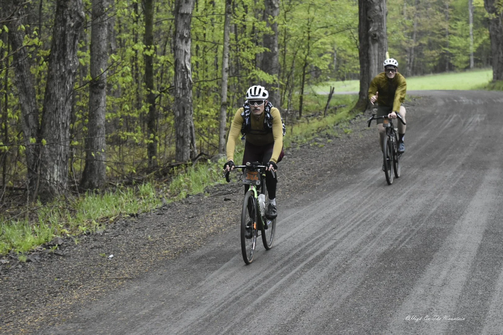 Two people riding bicycles on a dirt trail through a lush green forest.
