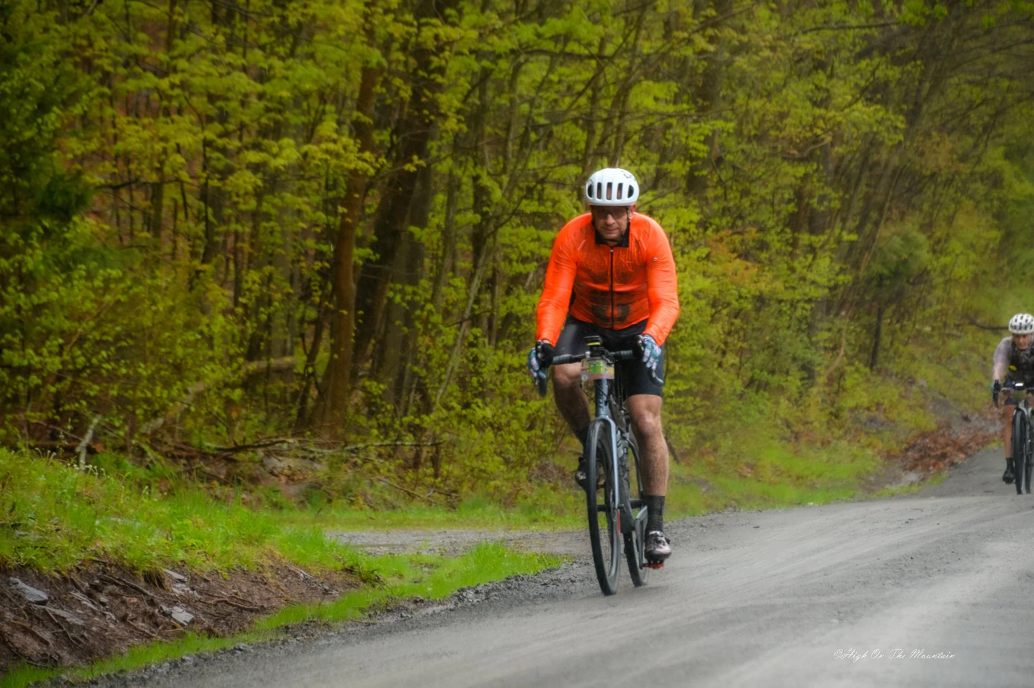 A man riding a mountain bike on a trail through a forested area with lush green trees.